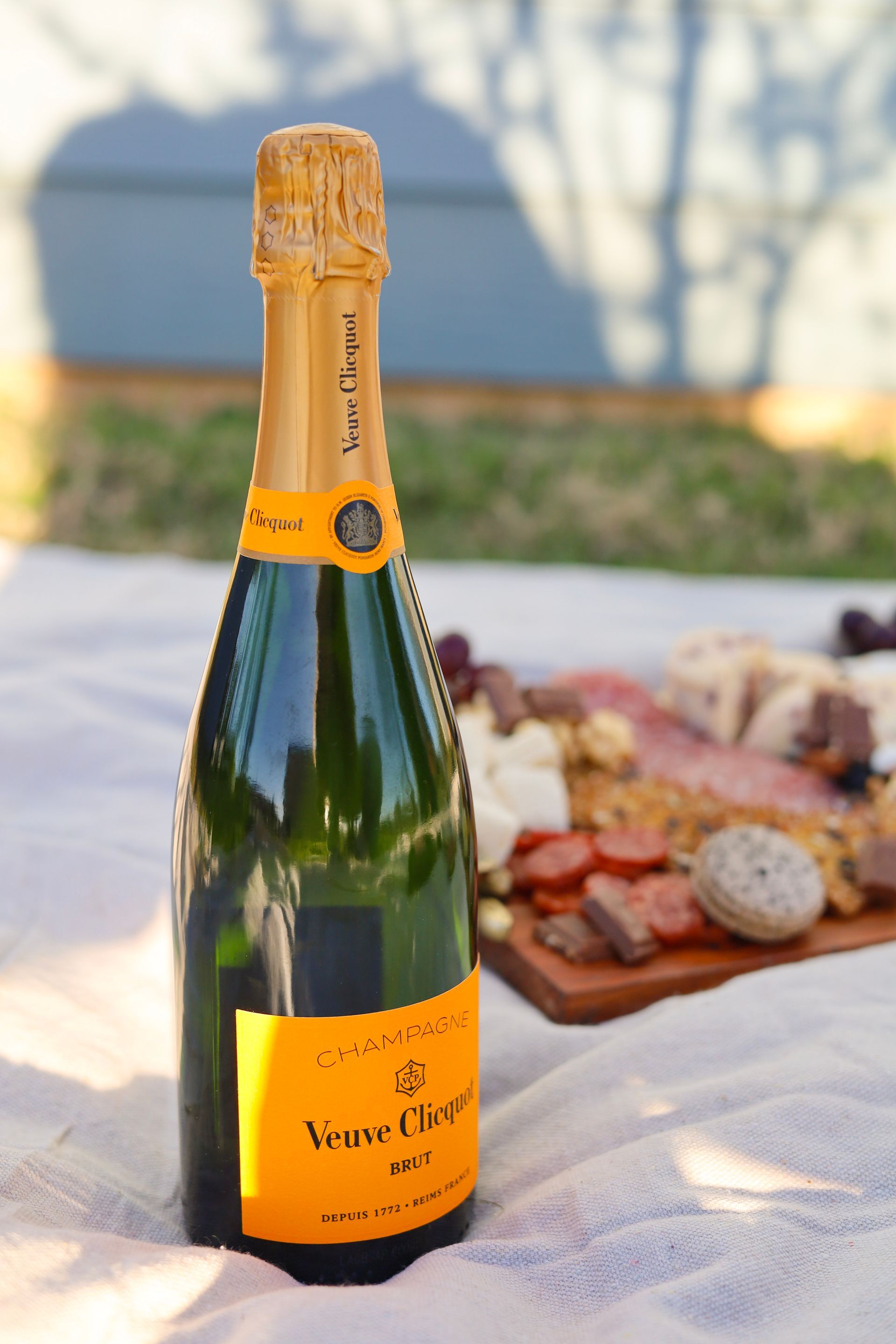 Champagne bottle on a picnic blanket with food in the background at sunset