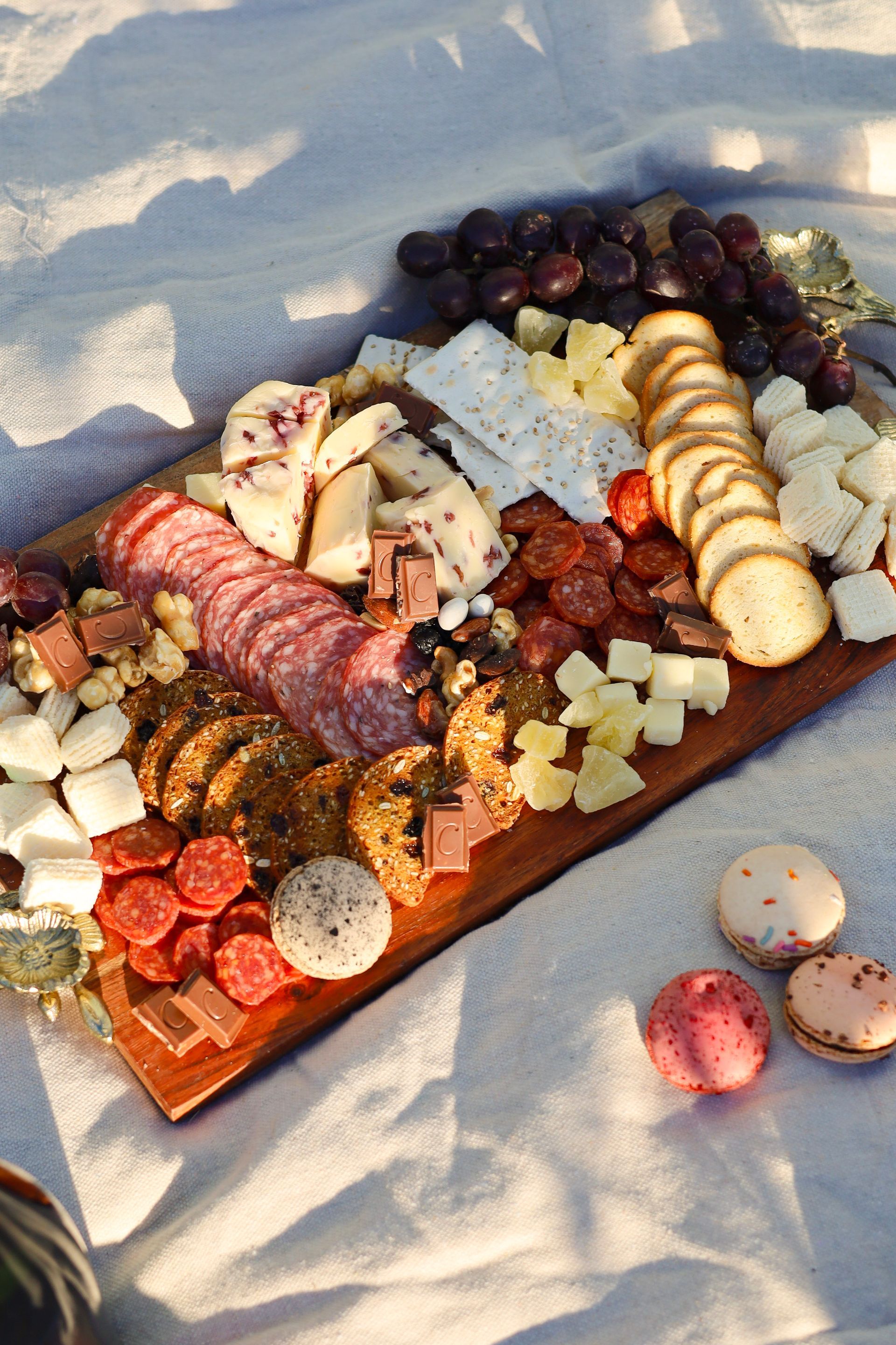 Charcuterie board with cheese, meats, fruit, and crackers on a blanket in warm sunlight