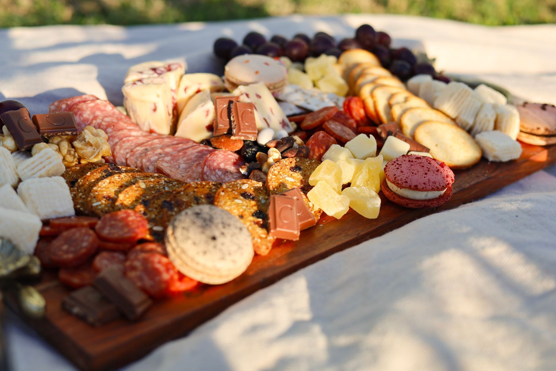 Assorted cheeses, charcuterie, fruit, and crackers arranged on a wooden board outdoors