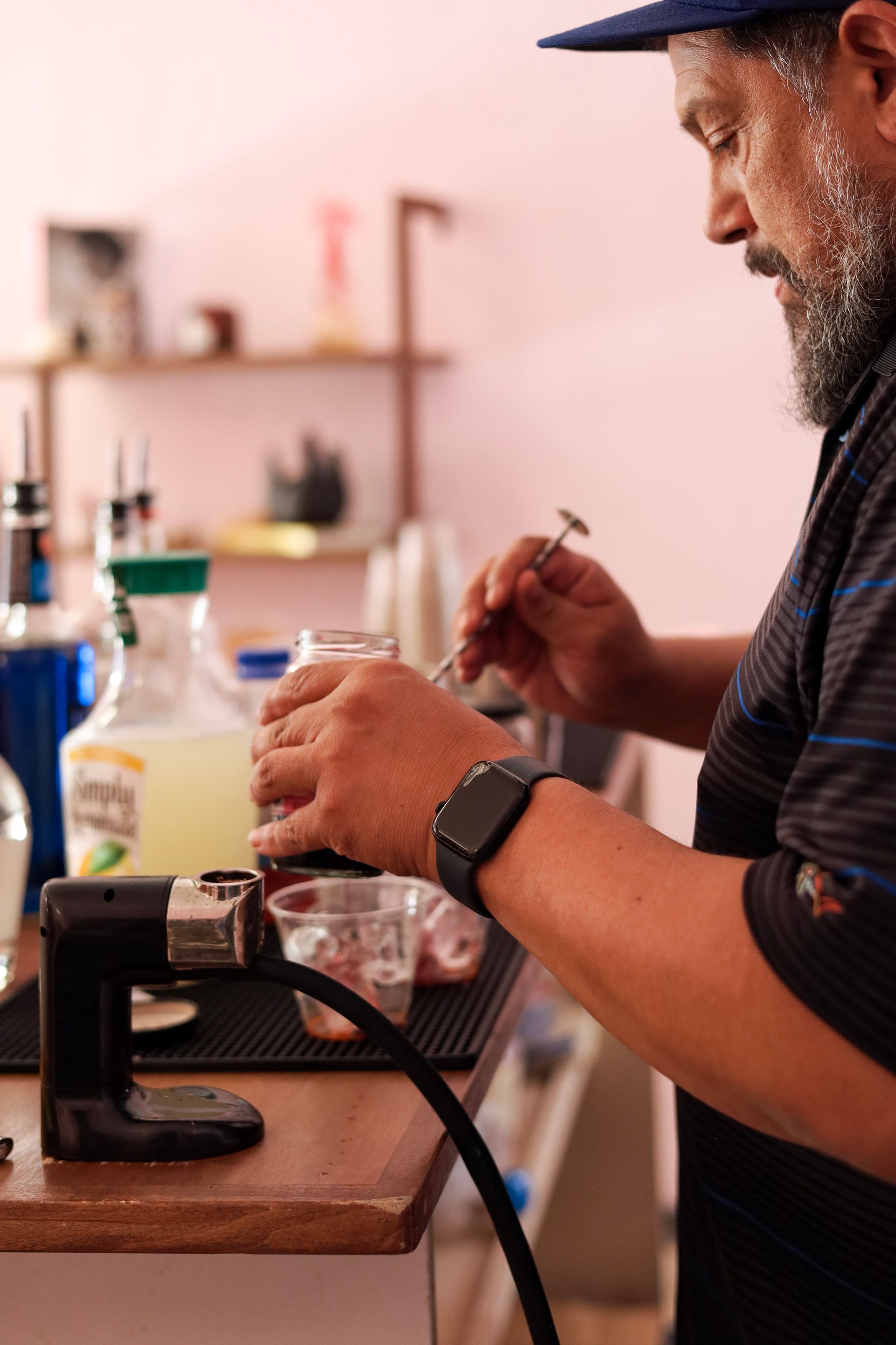 Person working with a small machine at a desk in a workshop, holding a tool and bottle.