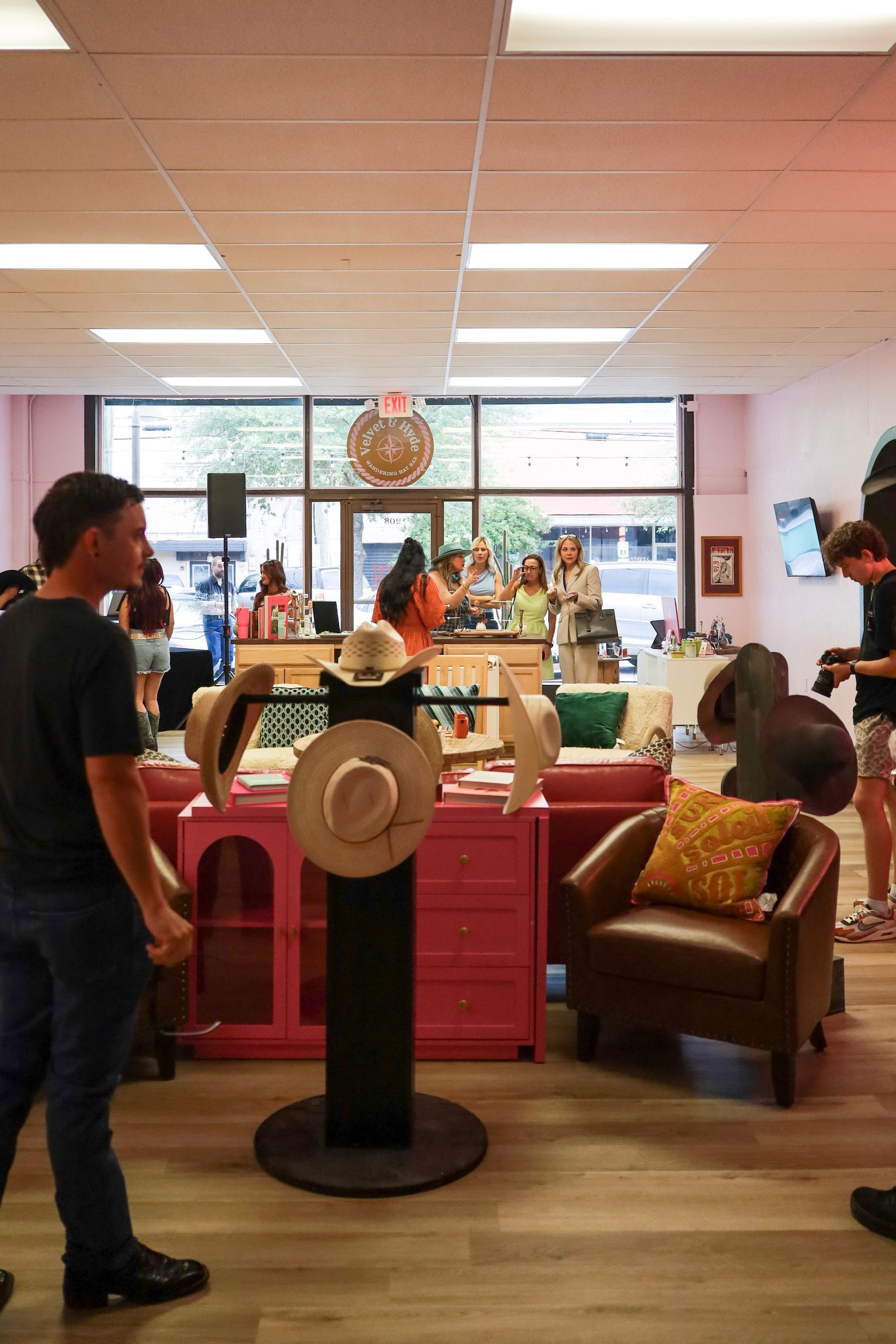 Indoor community room with people gathered around a central table and chairs, pink tablecloth, bright windows.