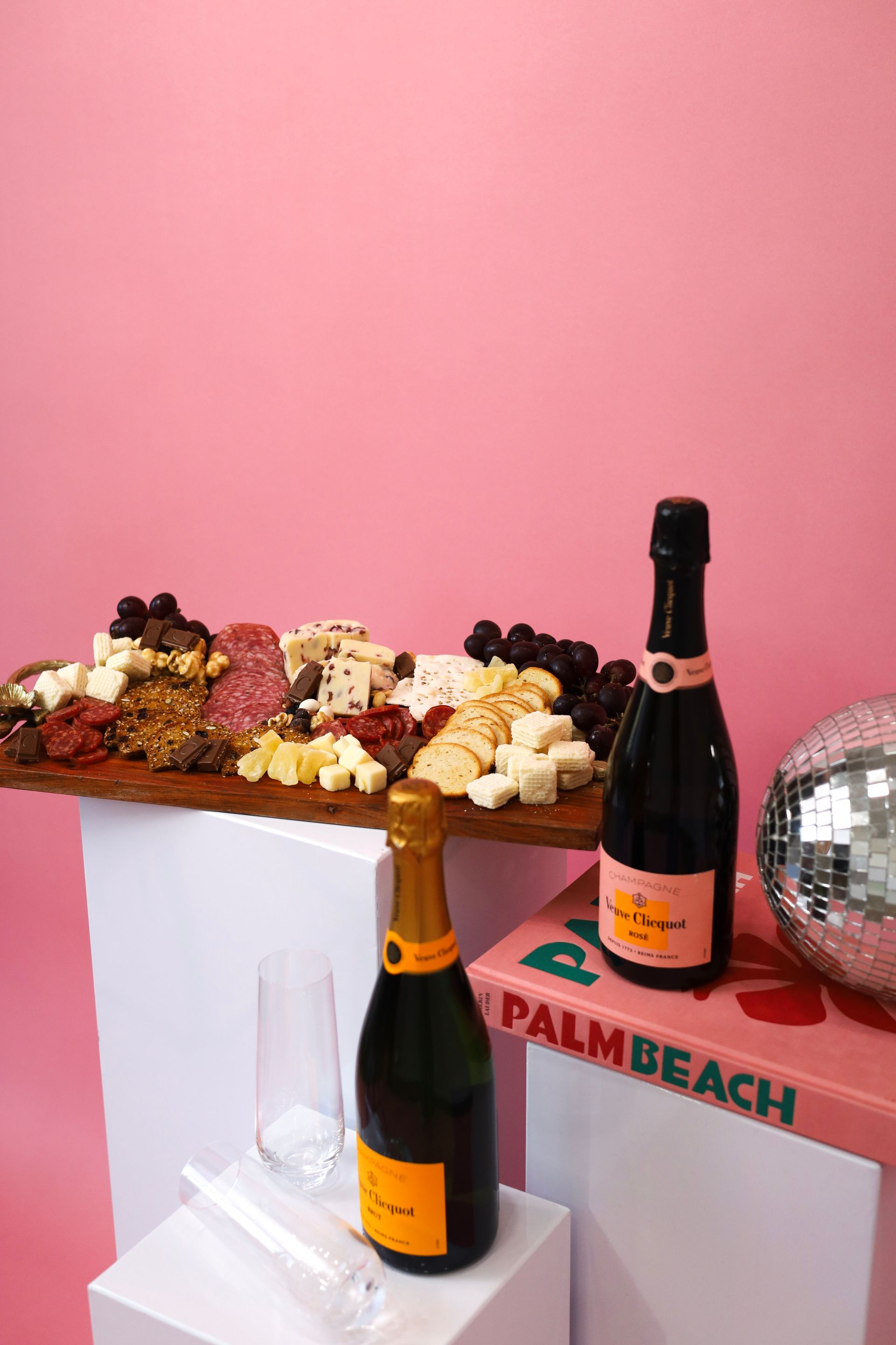 Champagne bottles and a fruit-topped dessert display on a white table against a pink backdrop.