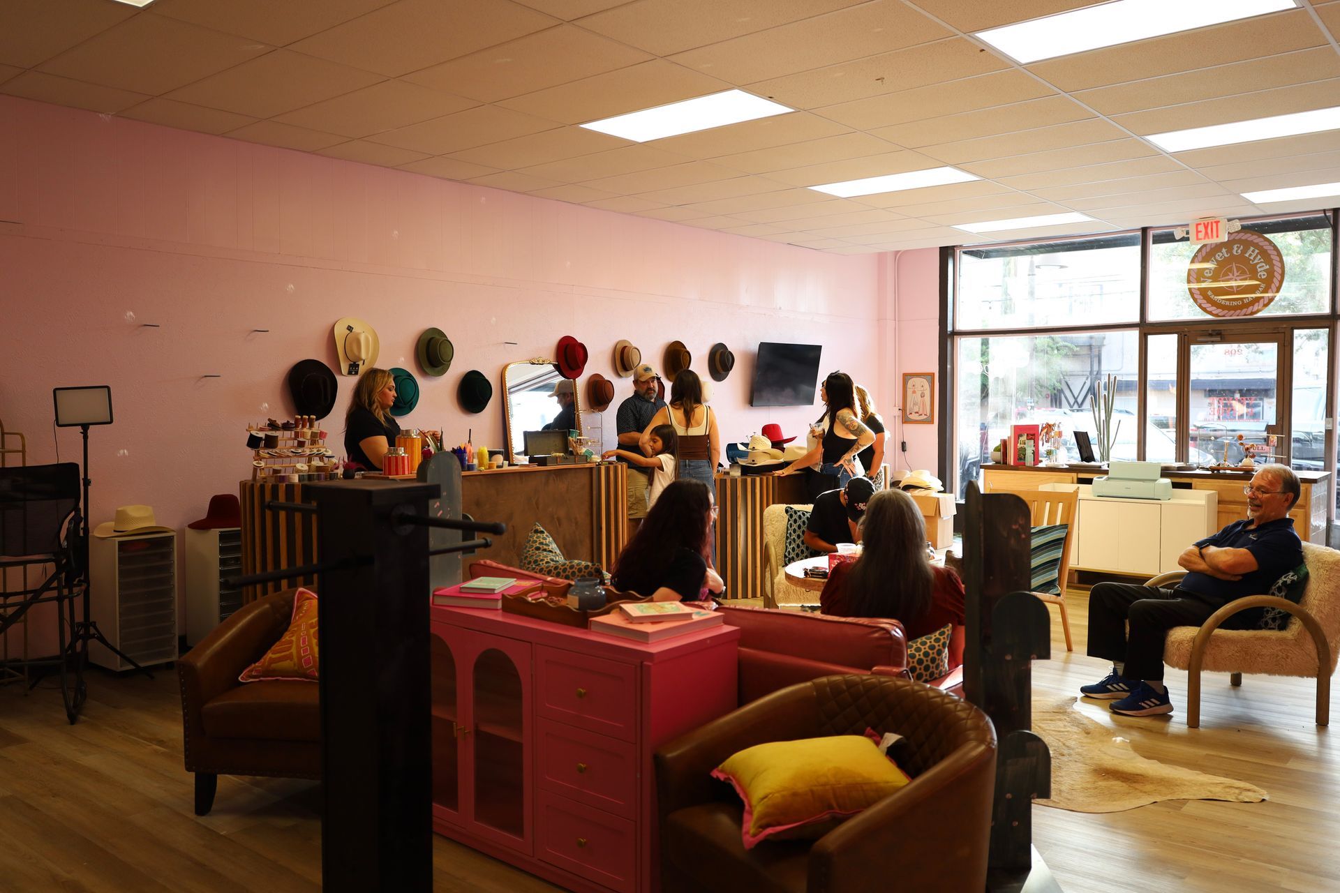 Hair salon with stylists and clients, pink walls, mirrors, and chairs in a bright room.