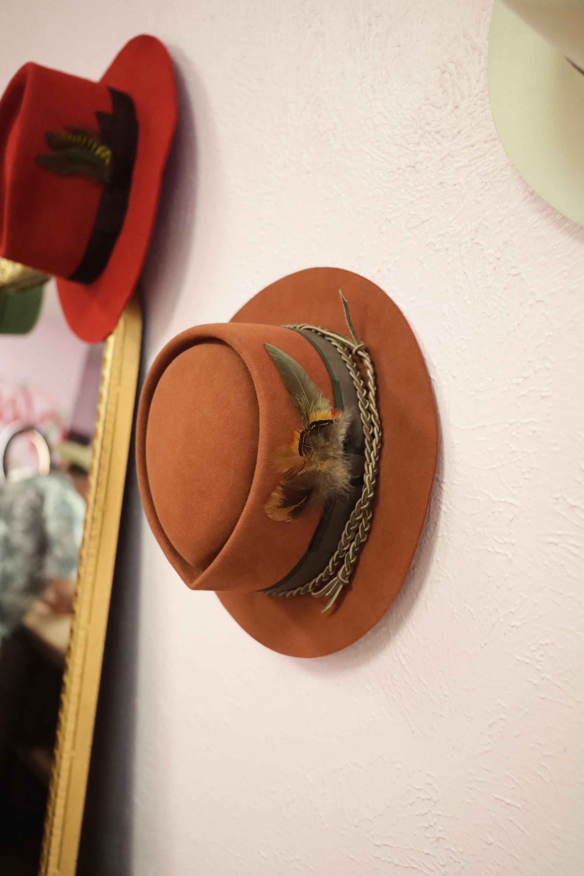 Orange hat hanging on a wall hook next to a red hat and mirror