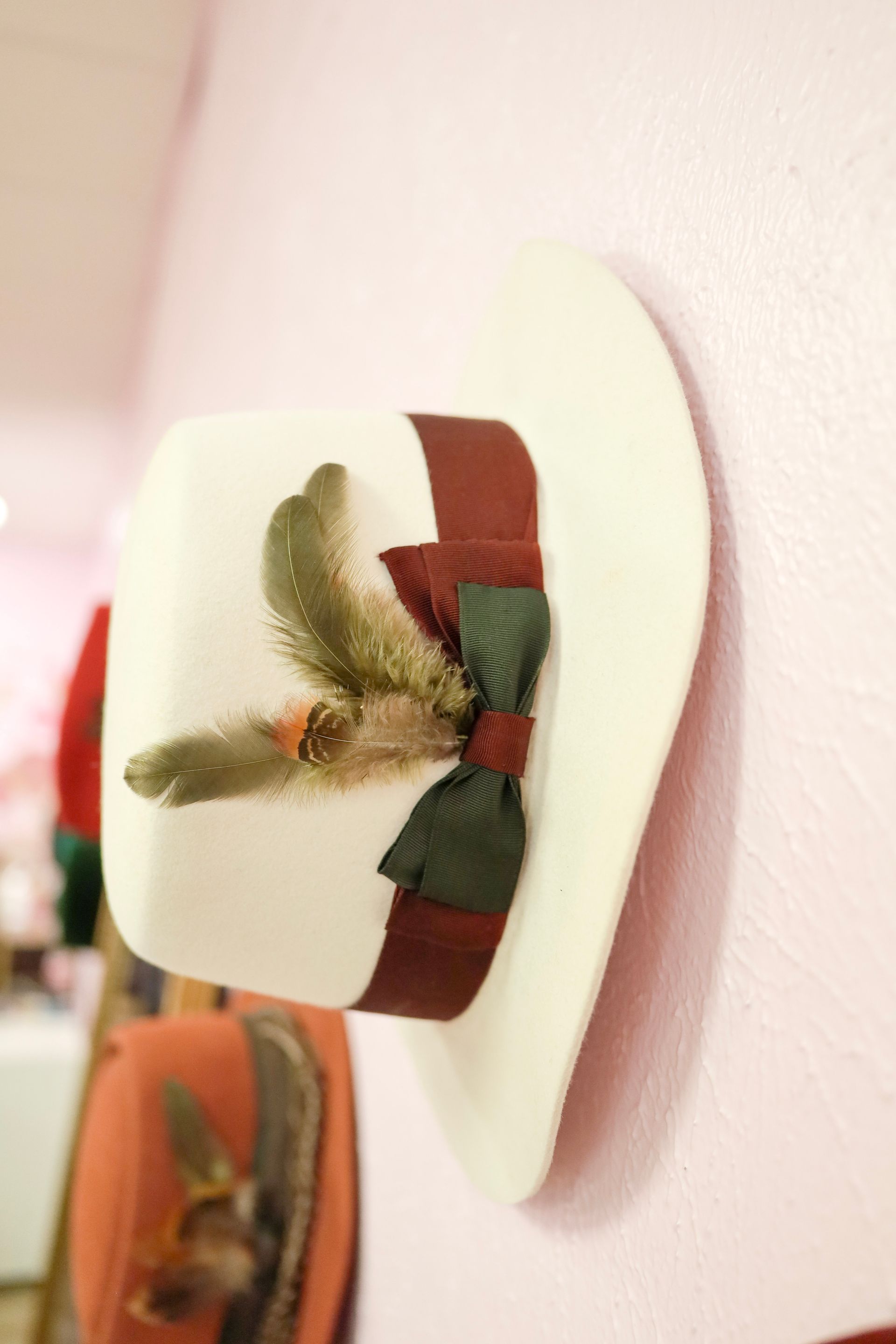 Decorative wall-mounted hair bow in cream, brown, and green on a pale pink wall