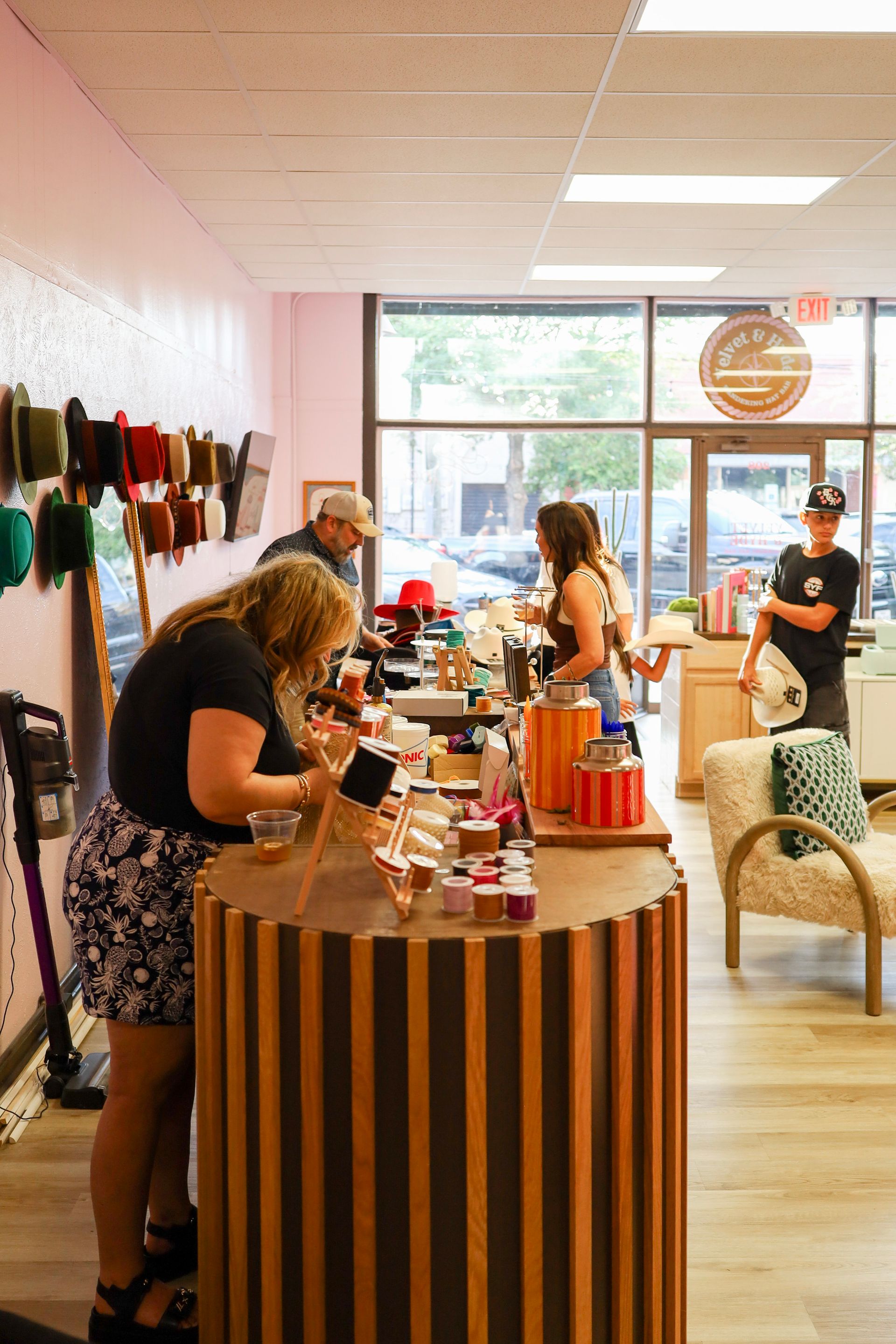 People browsing items at a small shop counter with shelves of colorful products and large front windows