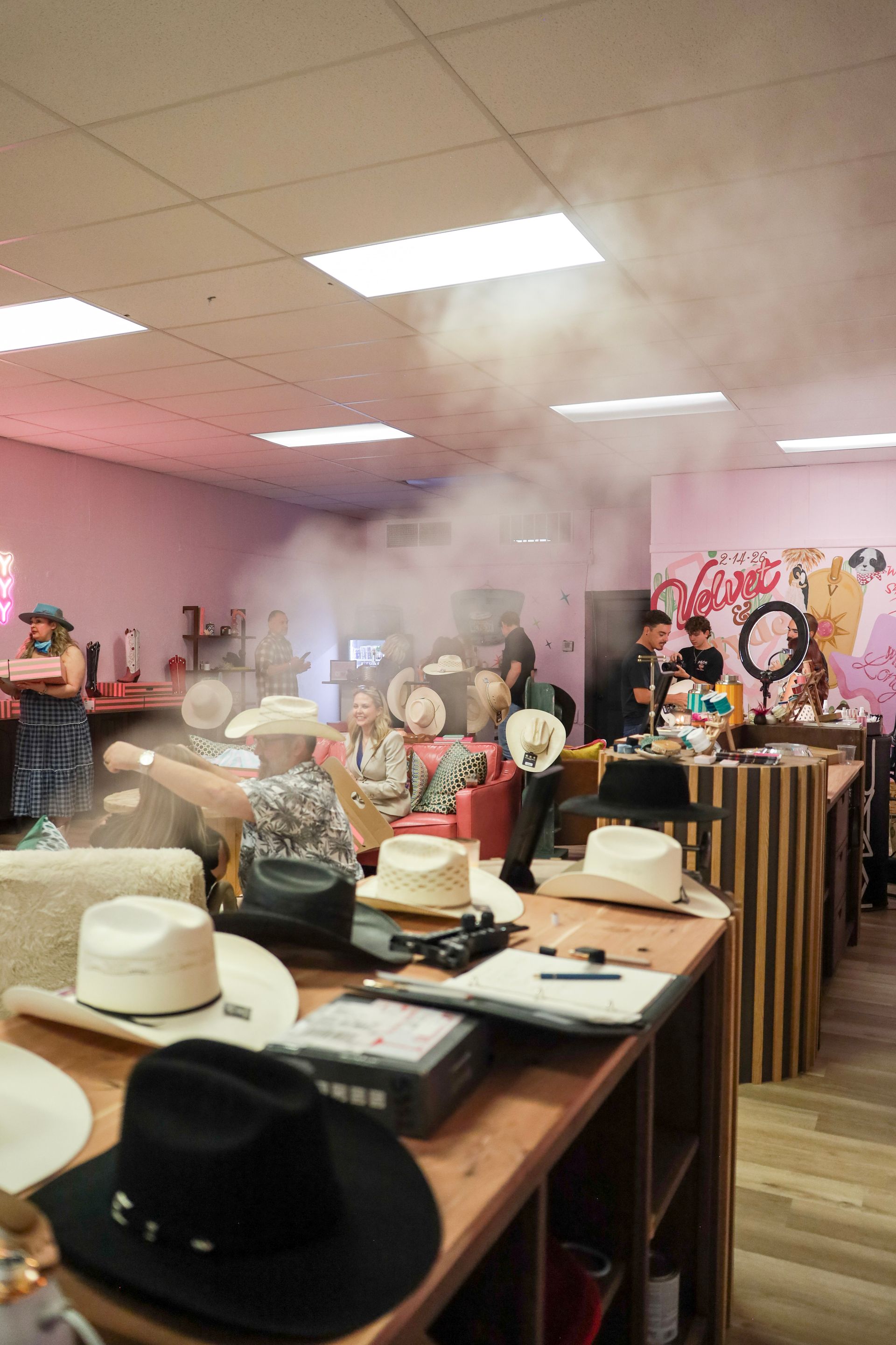 Hat display with many hats on tables in a shop, with a pink smoke haze and bright ceiling lights.