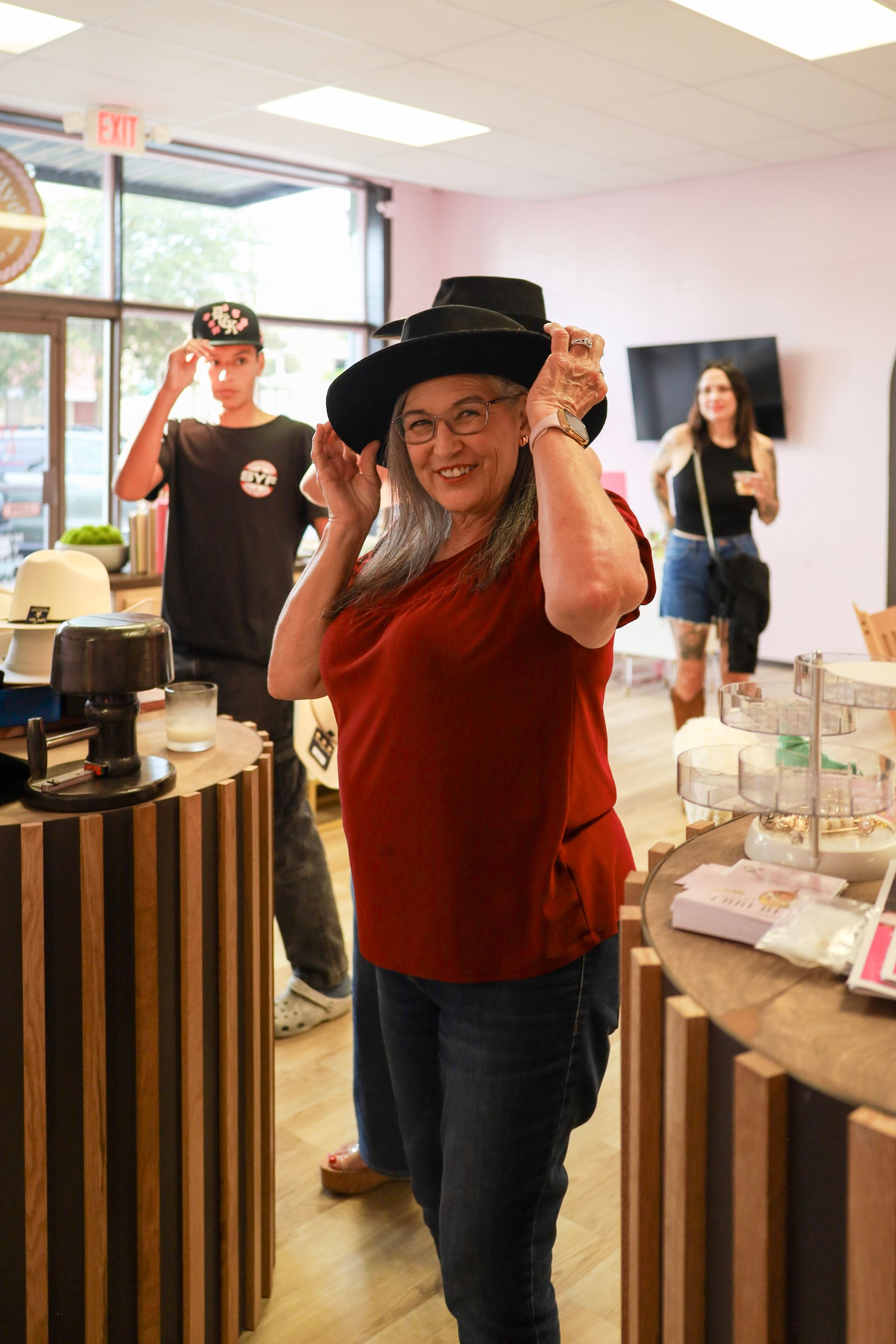 Person in red shirt and black hat smiling in a bright store, with two people in the background.