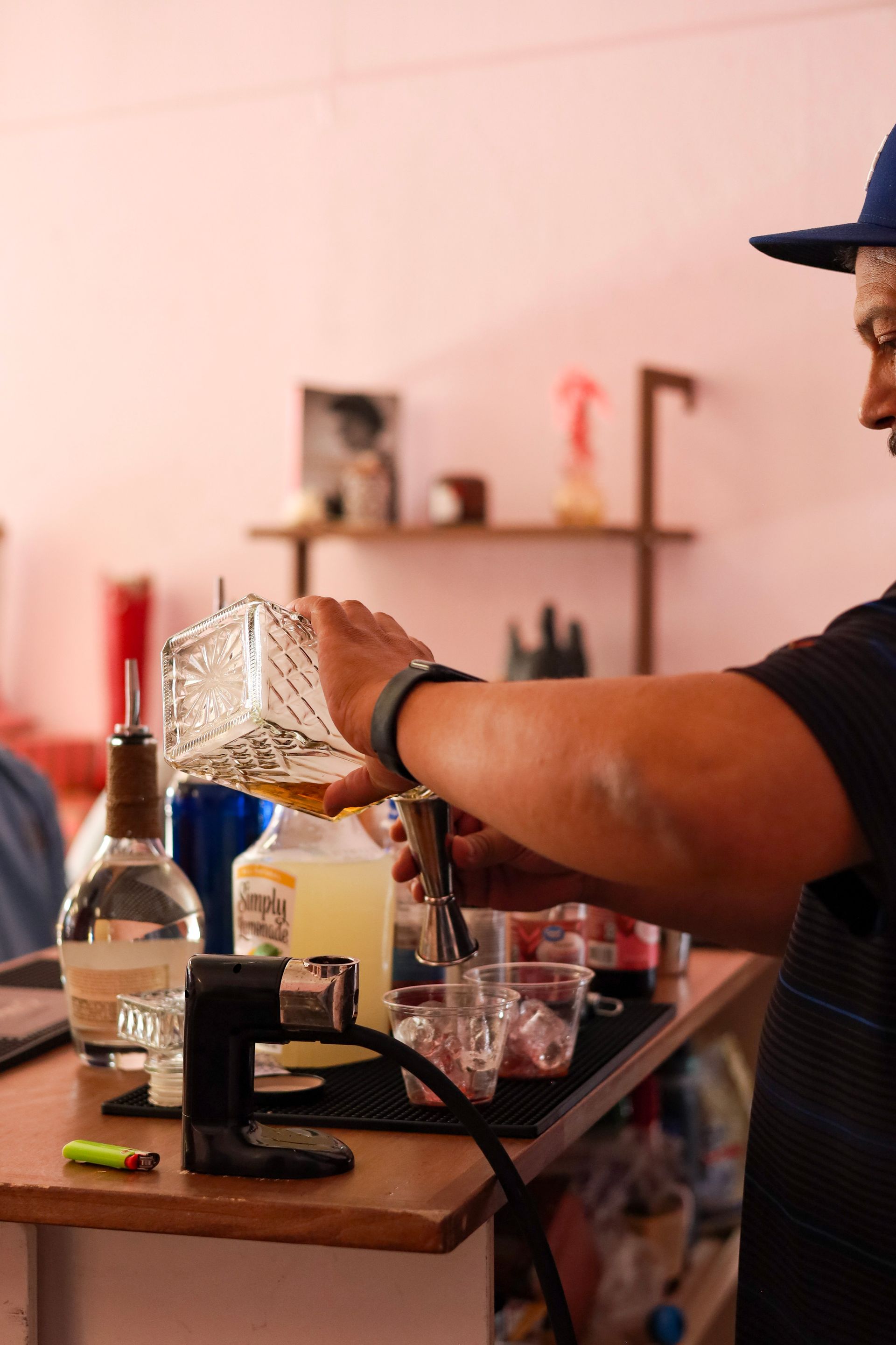 Person pouring a drink at a bar with bottles and glassware on the counter