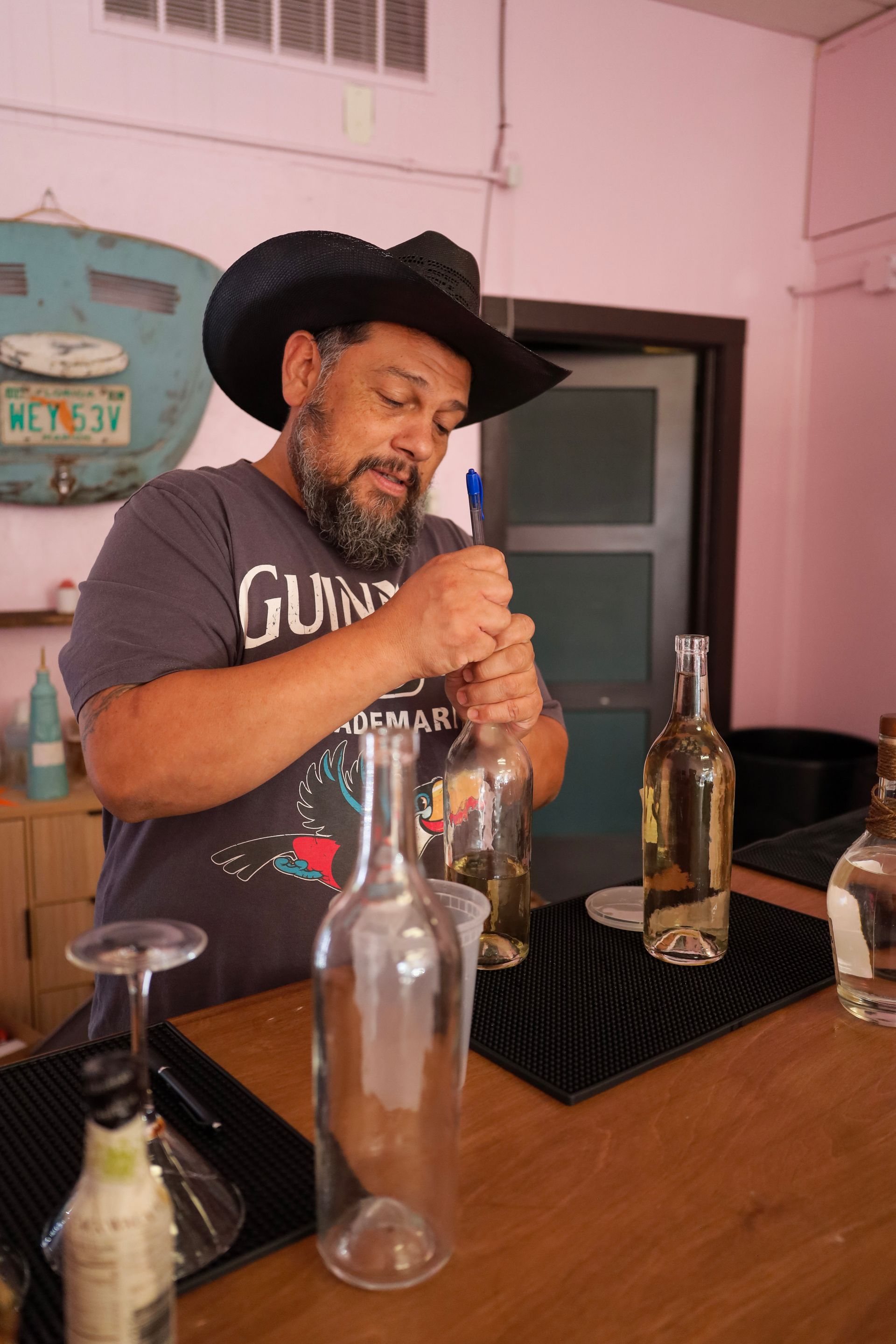 Man at a bar counter opening a bottle with several empty bottles nearby