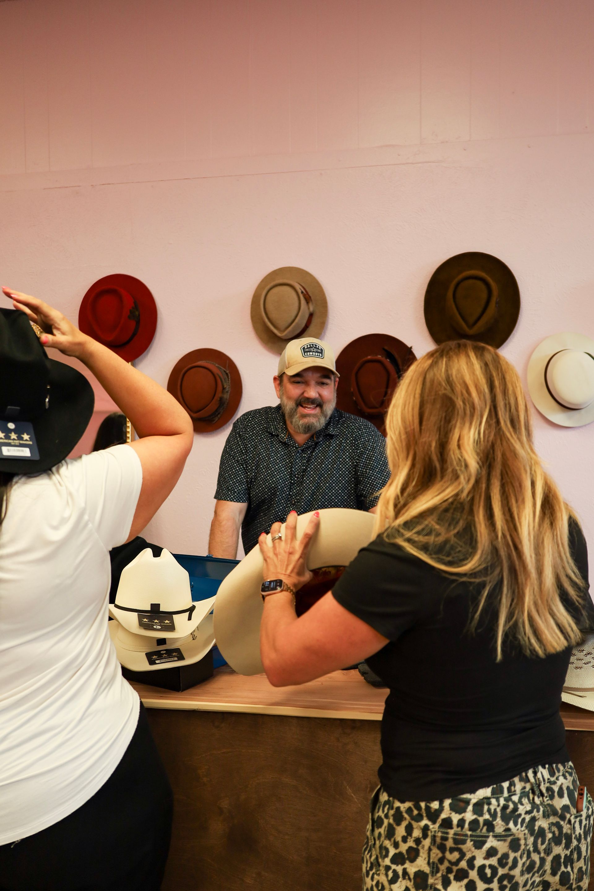 Person behind counter in a hat, with customers browsing cowboy hats on the wall.