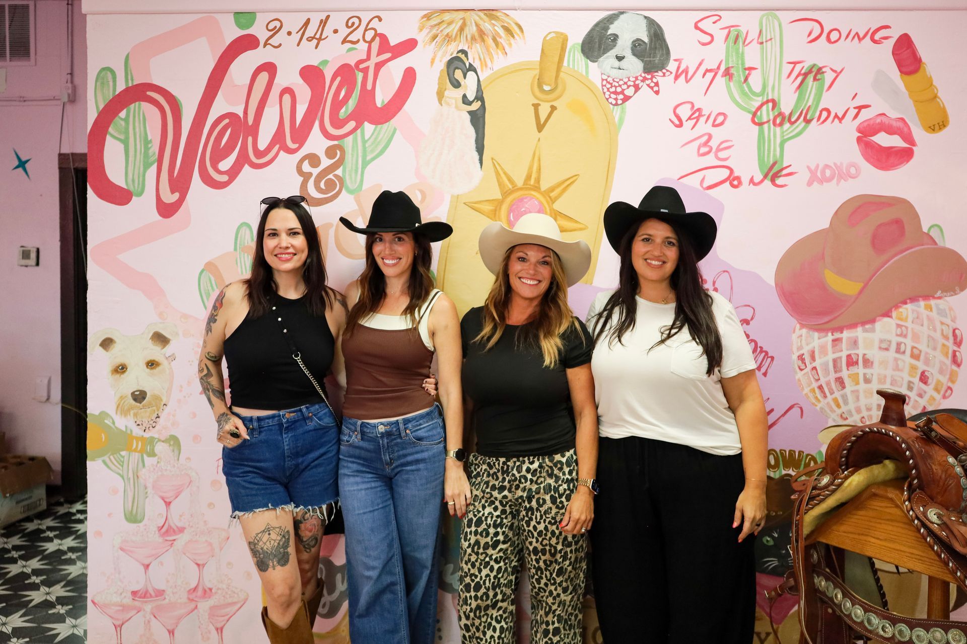 Four women pose in front of a pink 