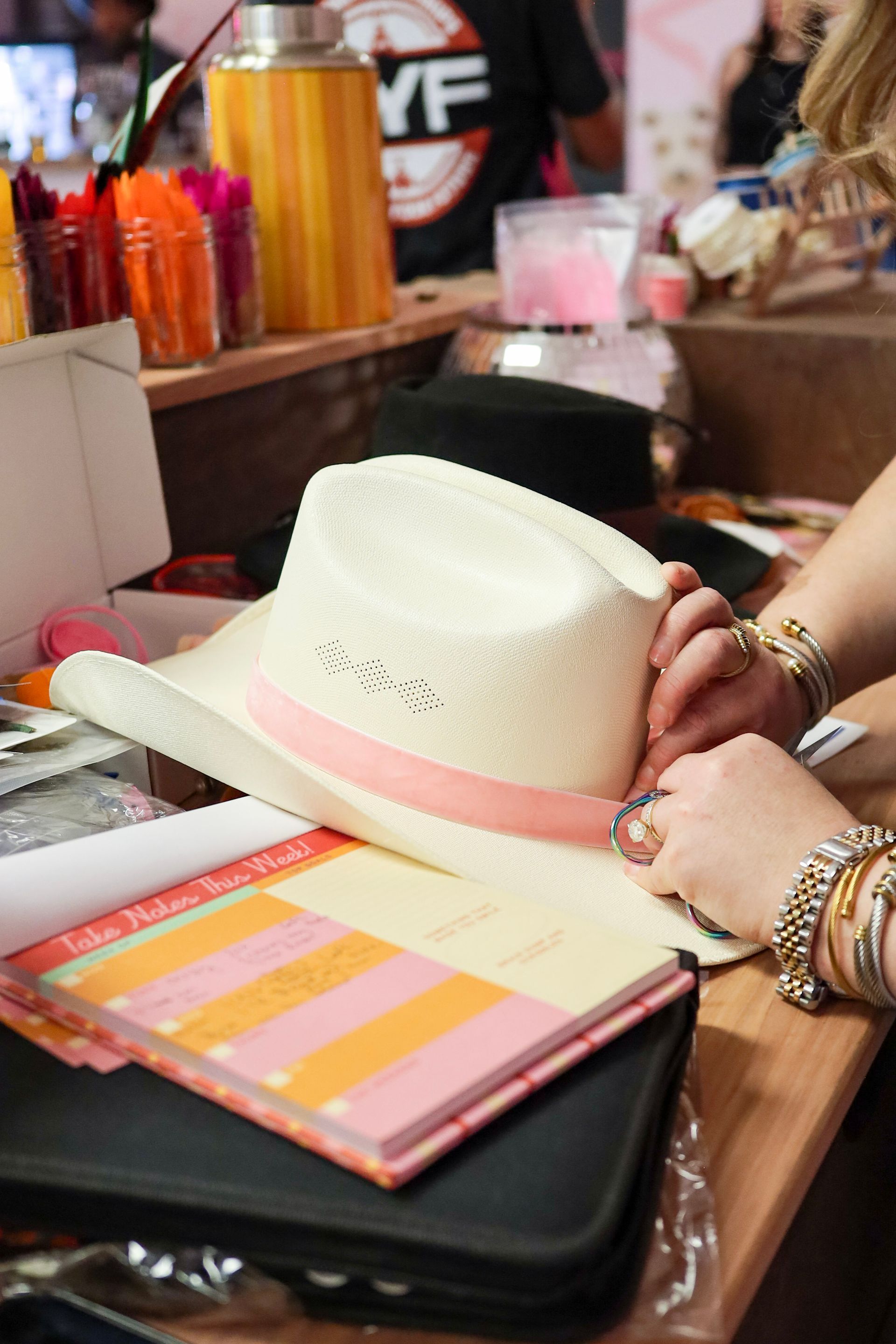 Hands adjusting a white sunhat on a table with colorful notebooks and accessories