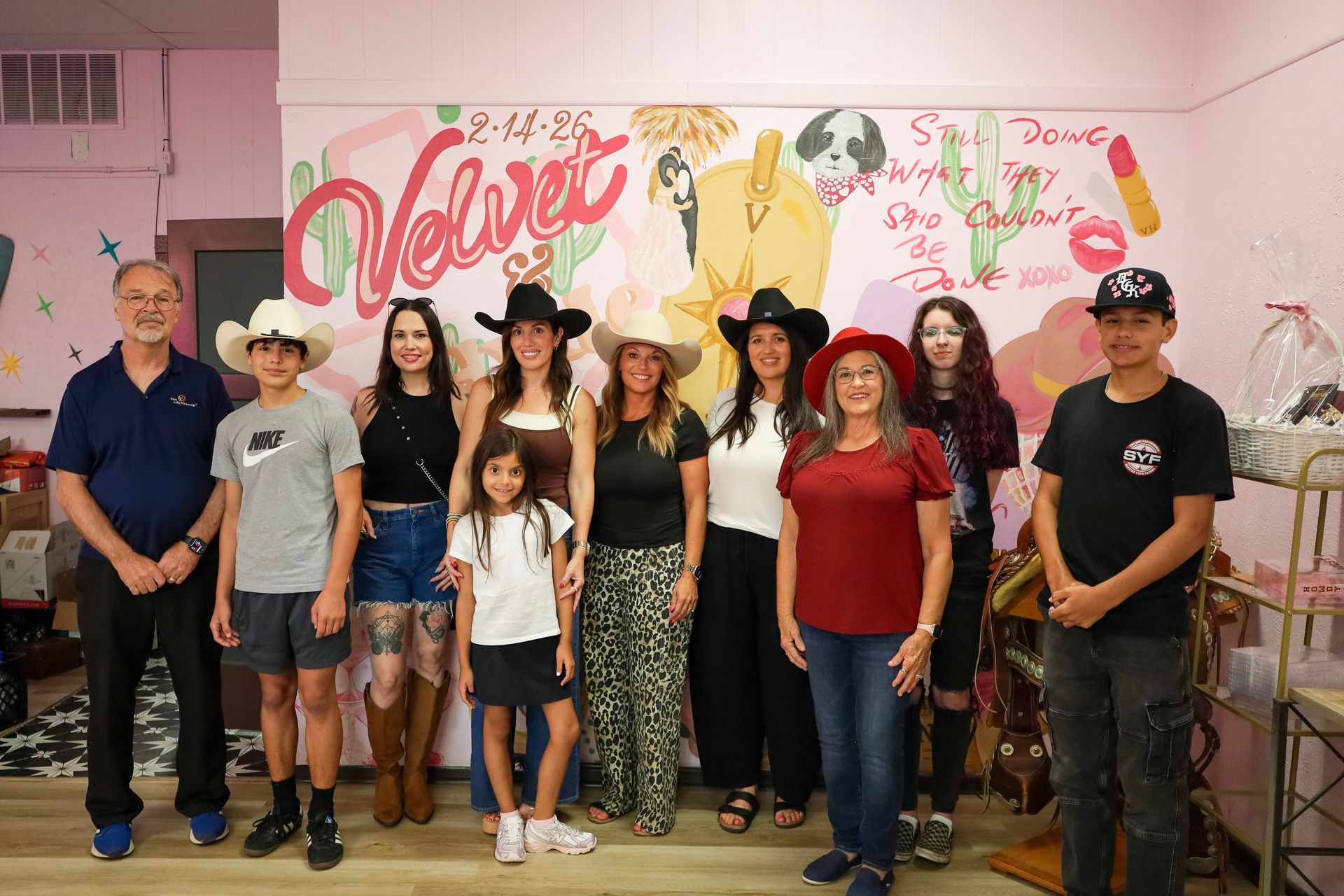 Group of people posing indoors in front of a pink “Believe” mural at a celebration event