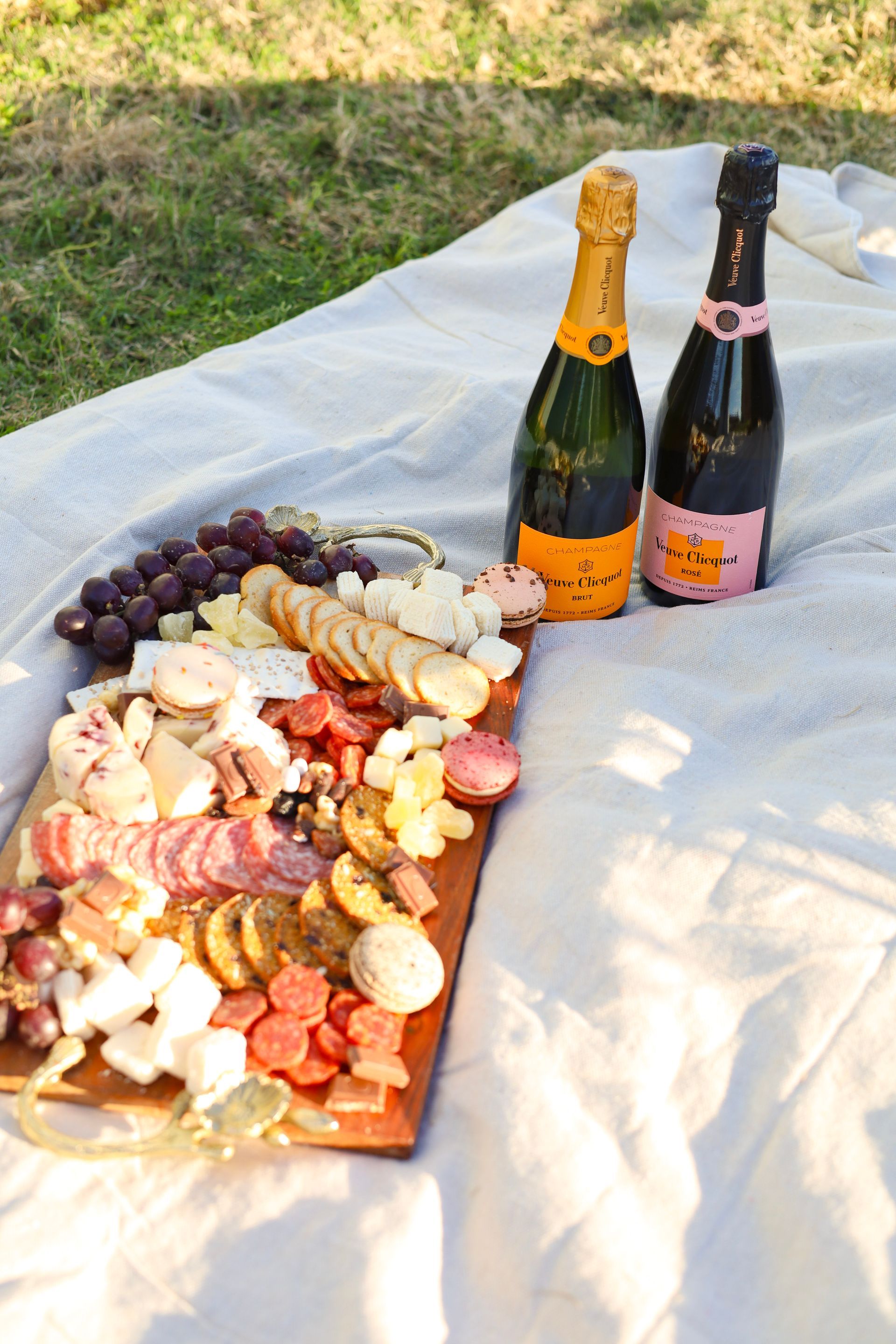 Picnic spread with fruit and snacks on a blanket beside two bottles of sparkling wine outdoors