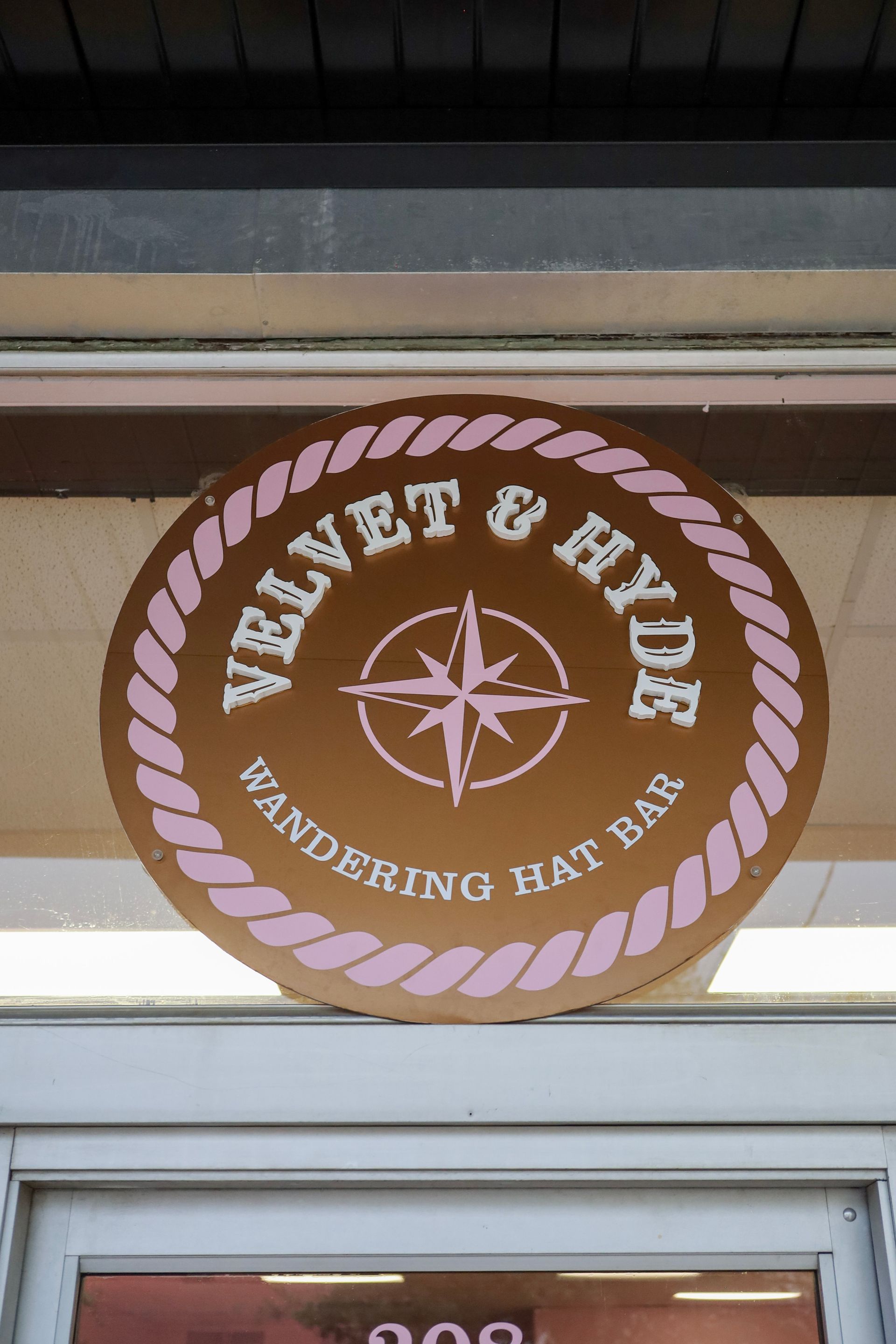 Brown circular Velvet & Hyde sign with white compass and rope border above a storefront, reading “Pandering Bat Bar”
