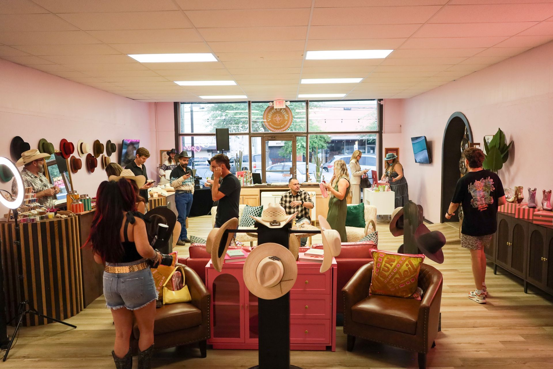 Clothing store interior with shoppers browsing racks and pink chairs in a bright showroom