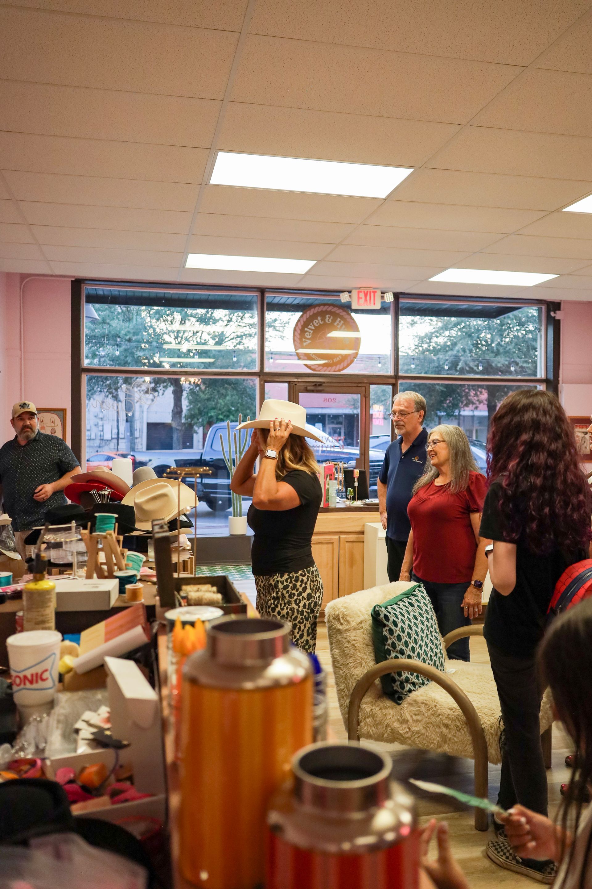 People gathered inside a cafe-like room near a counter, with large windows and trays of drinks.