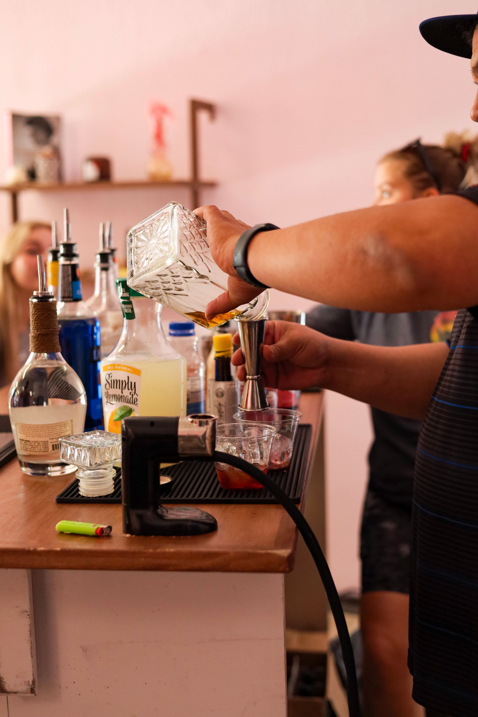 Person pouring liquid into a glass at a cluttered home bar with bottles and drinks on the counter
