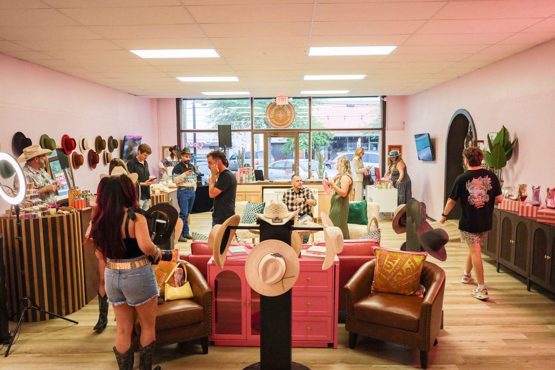 Clothing boutique with racks of dresses, pink chairs, and shoppers browsing under bright lights.