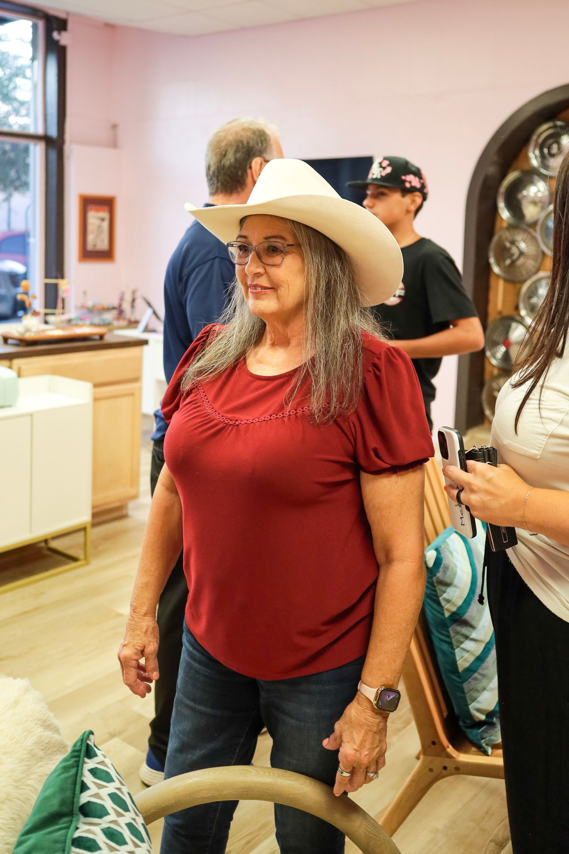 Woman in white hat and red top standing indoors among other people
