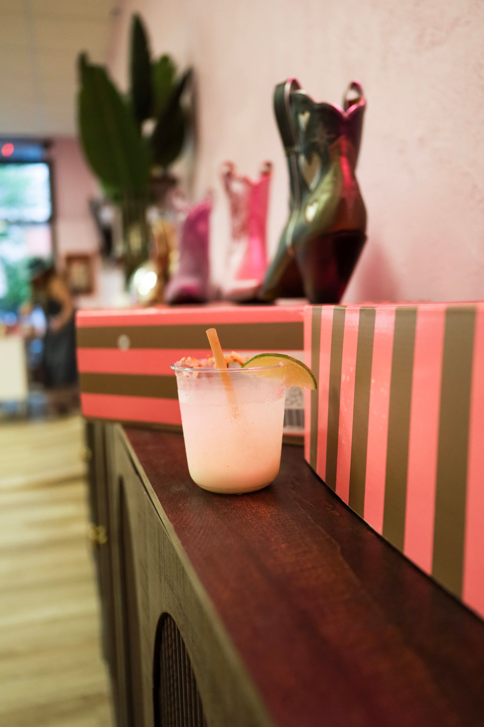 Small pink drink with straw on a shelf beside striped pink-and-brown decor and shoes