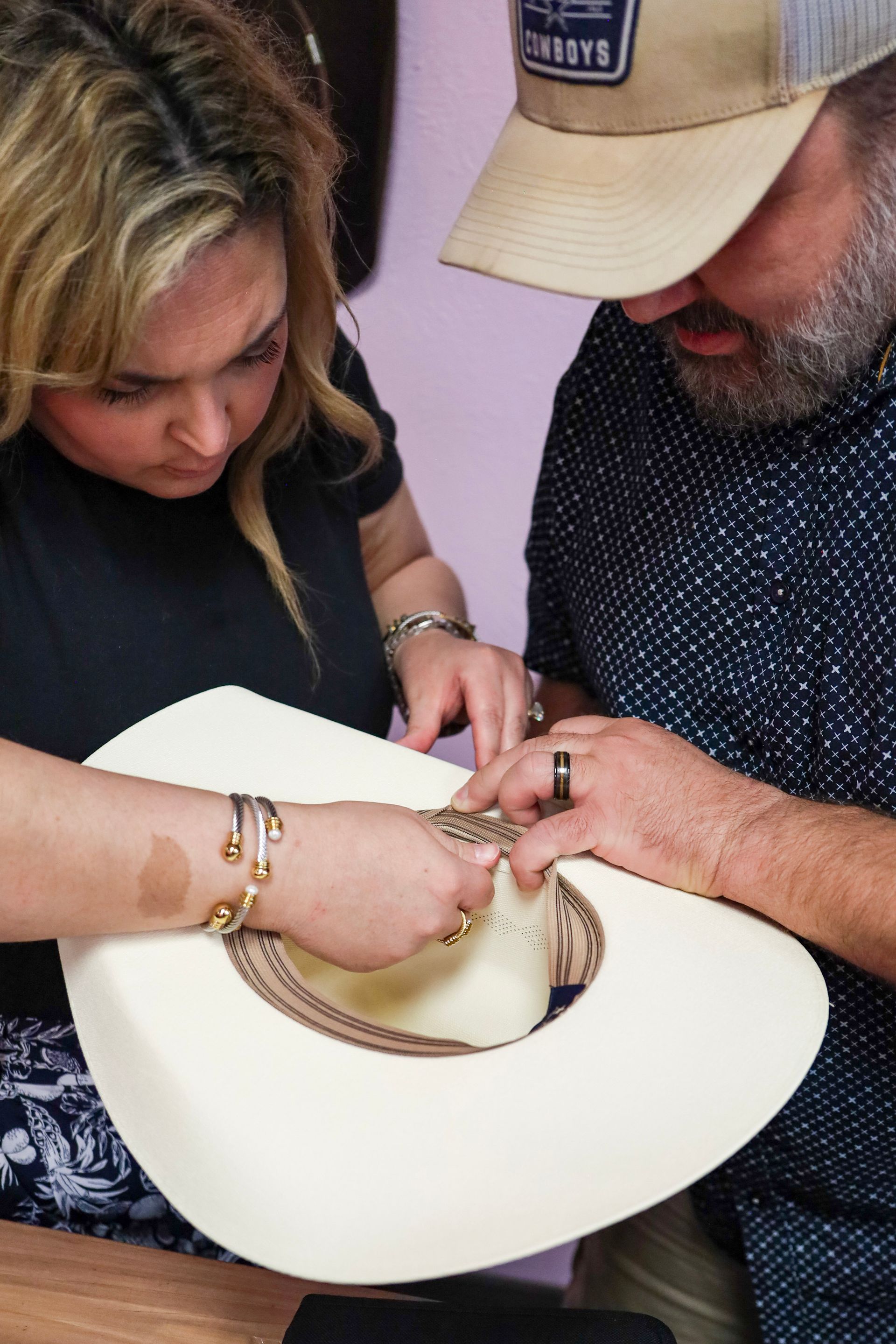 Two people examining a white cowboy hat together indoors