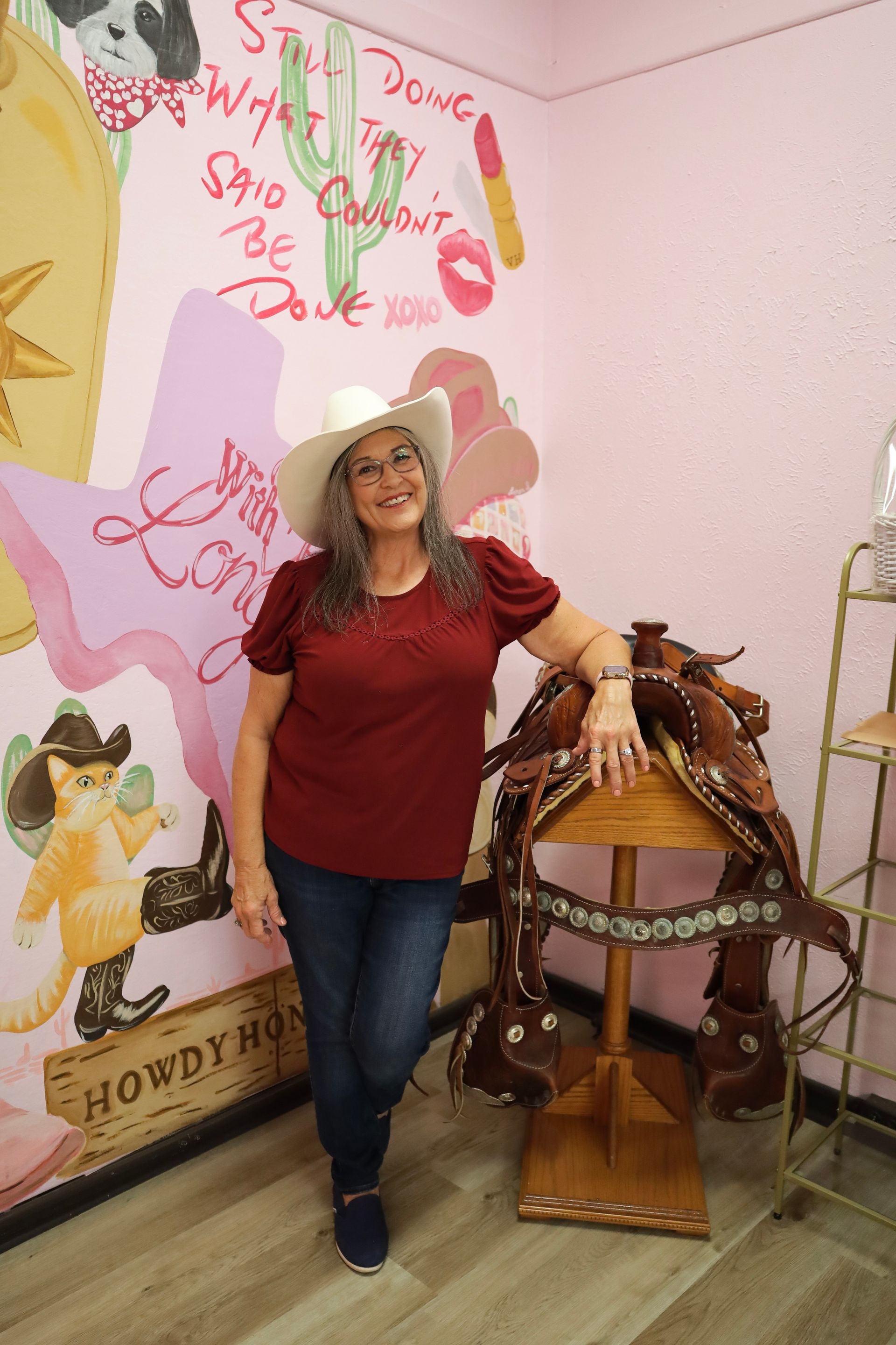 Woman in a red shirt and hat standing beside a decorated carousel horse in a colorful room
