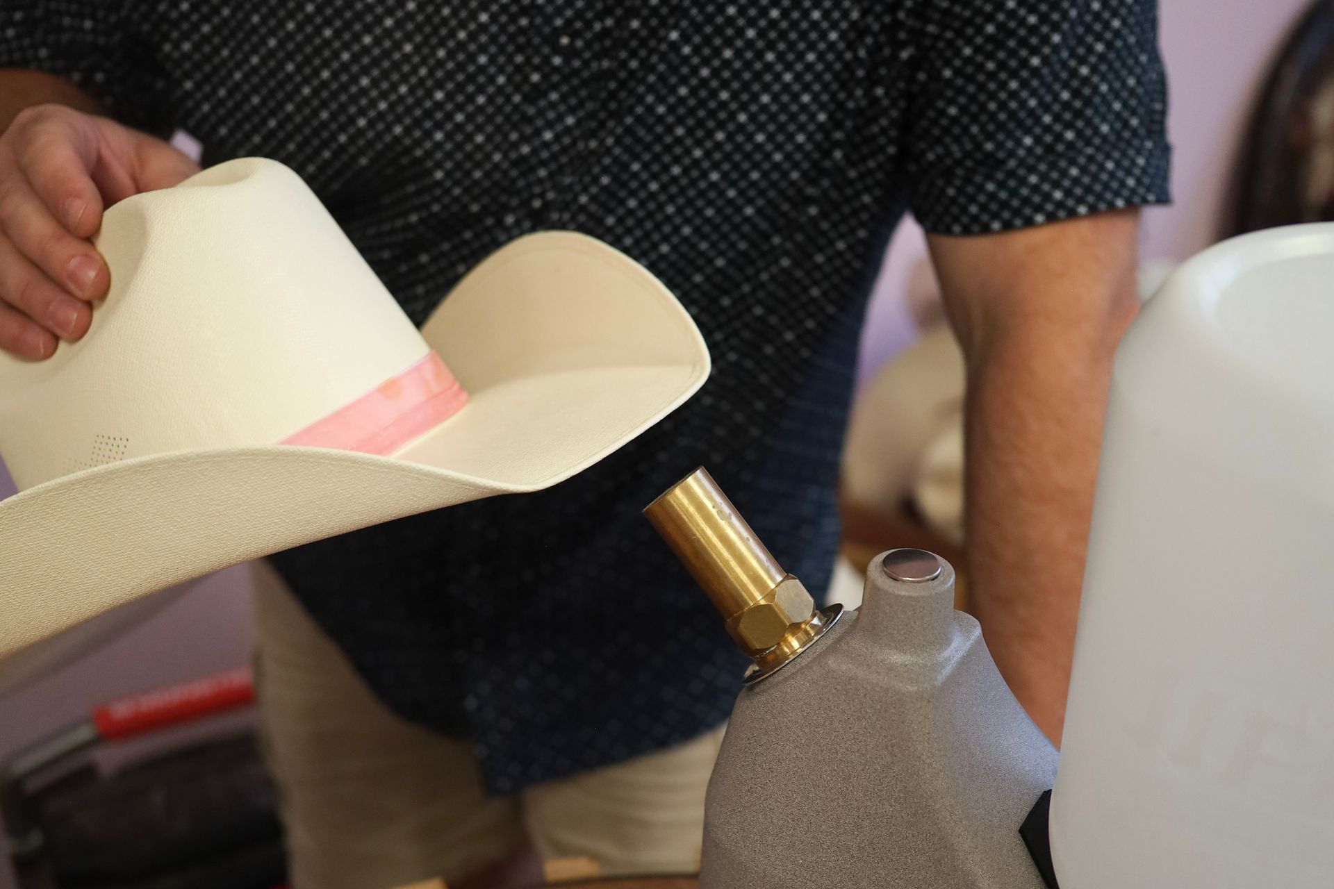Person holding a white cowboy hat near a small torch and propane tank in a workshop setting
