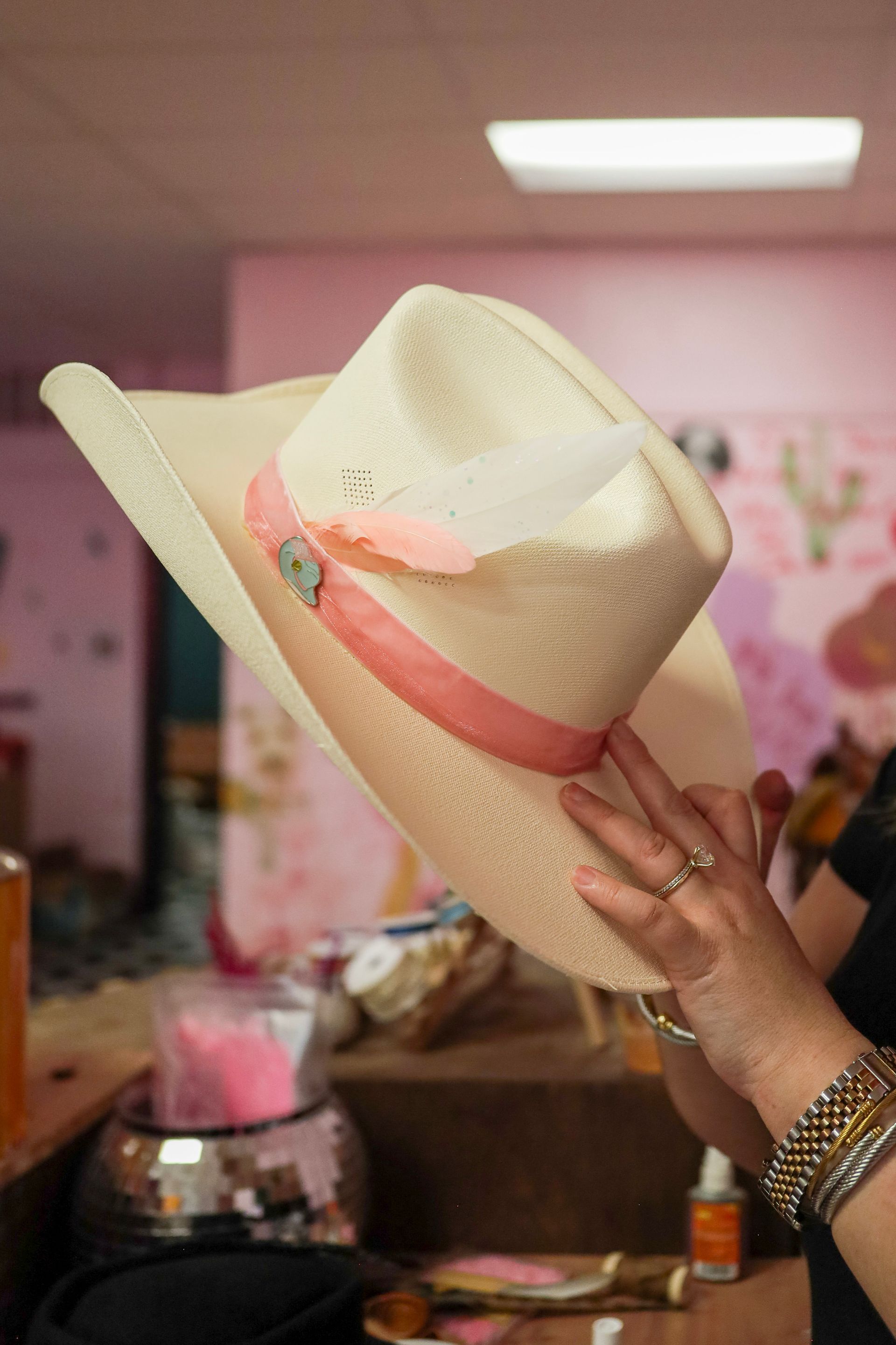 Hand holding a white straw hat with a pink ribbon in a pink room