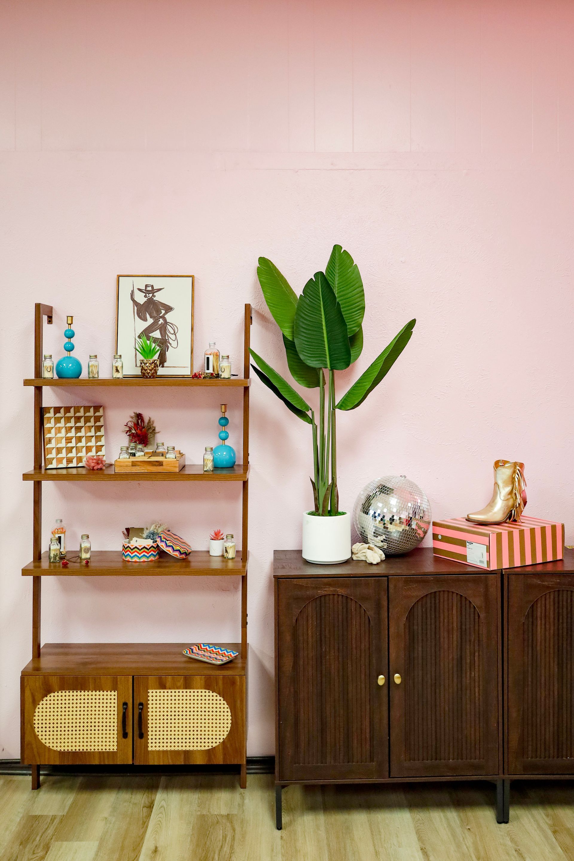 Wooden shelves and cabinet with decor and plants against a pink wall