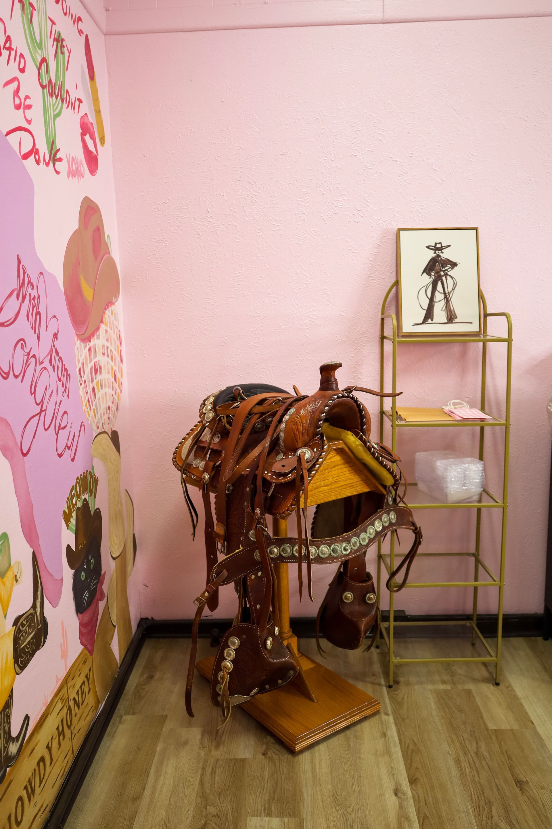 Leather saddle on a stand beside a small gold shelf against a pink wall