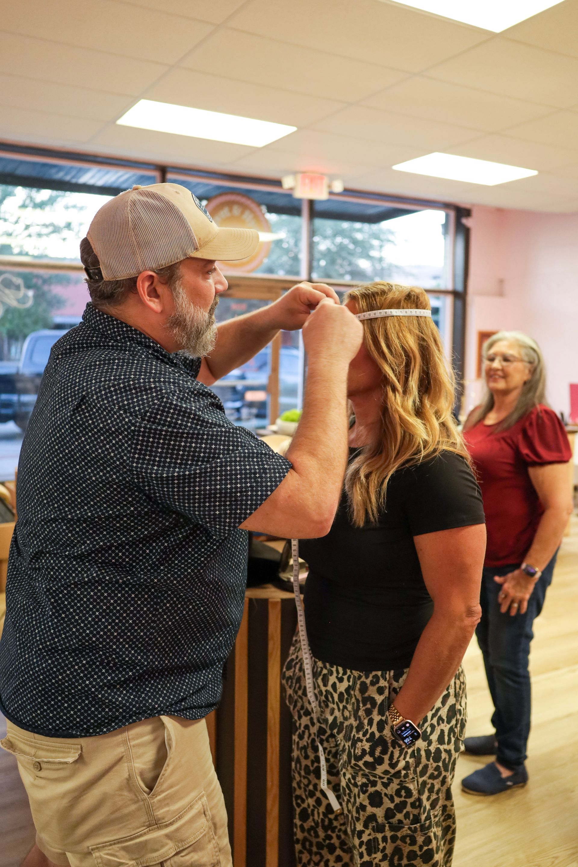 A man measures a woman’s height indoors while another woman watches nearby.