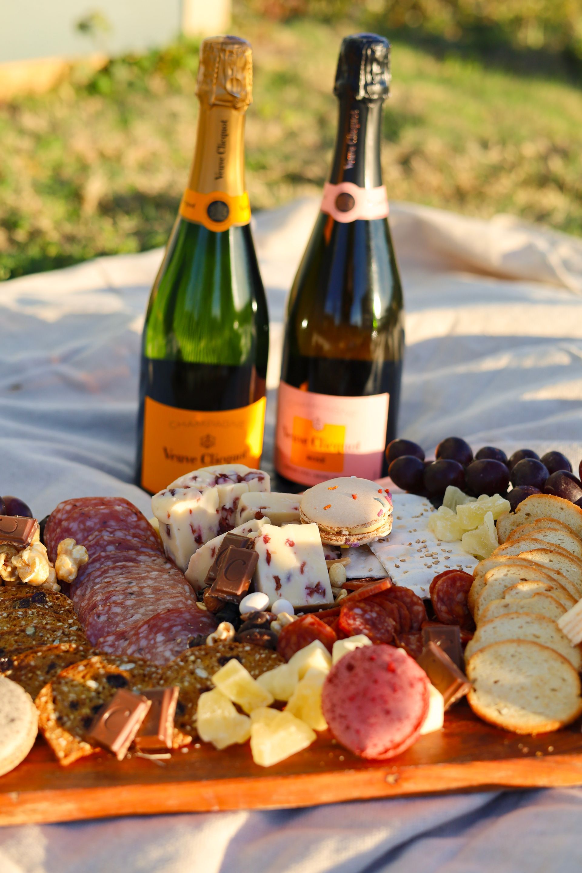 Charcuterie board with cheeses, sliced meats, grapes, and two champagne bottles outdoors