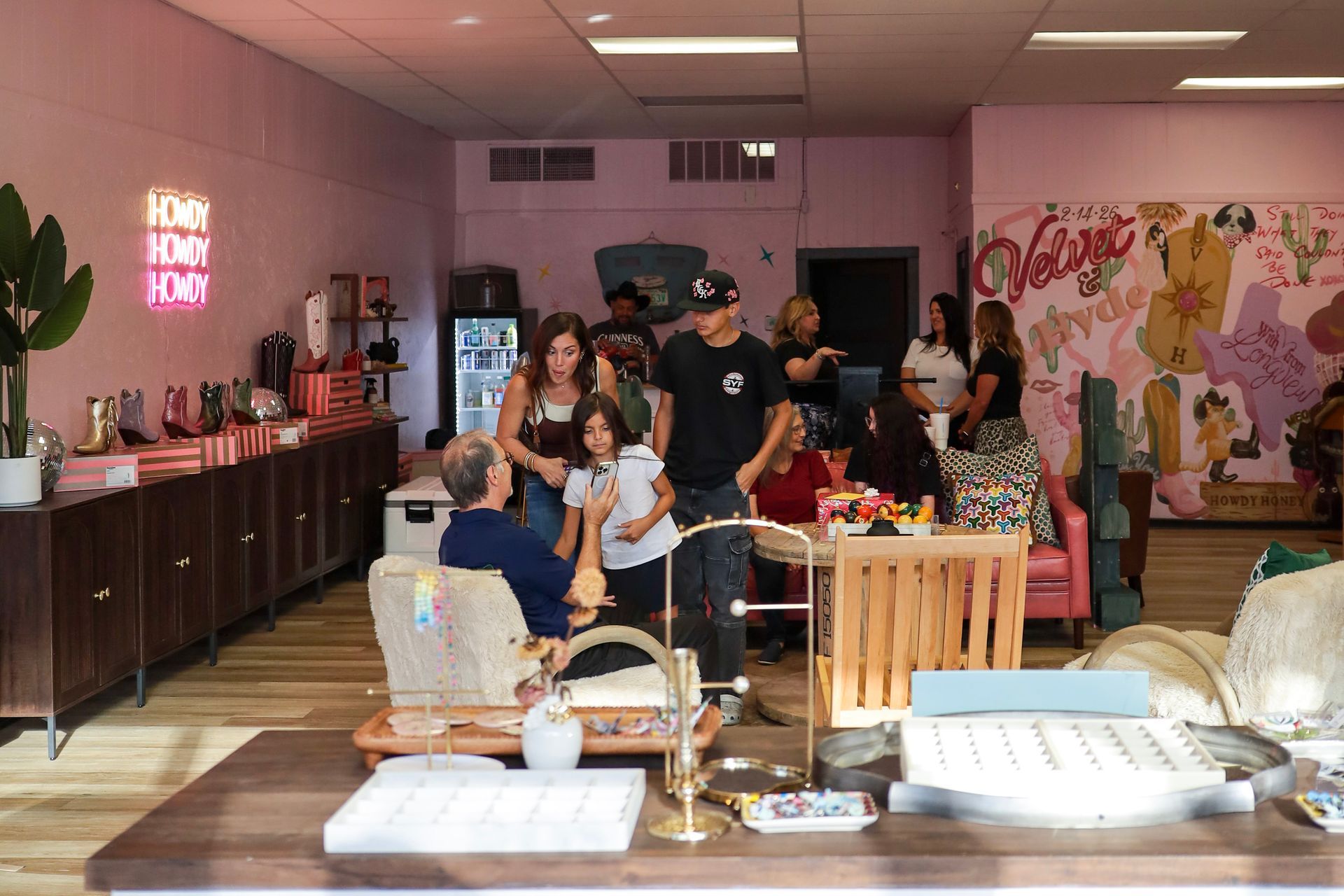 People gathered around a dessert display inside a pink-walled bakery or cafe.
