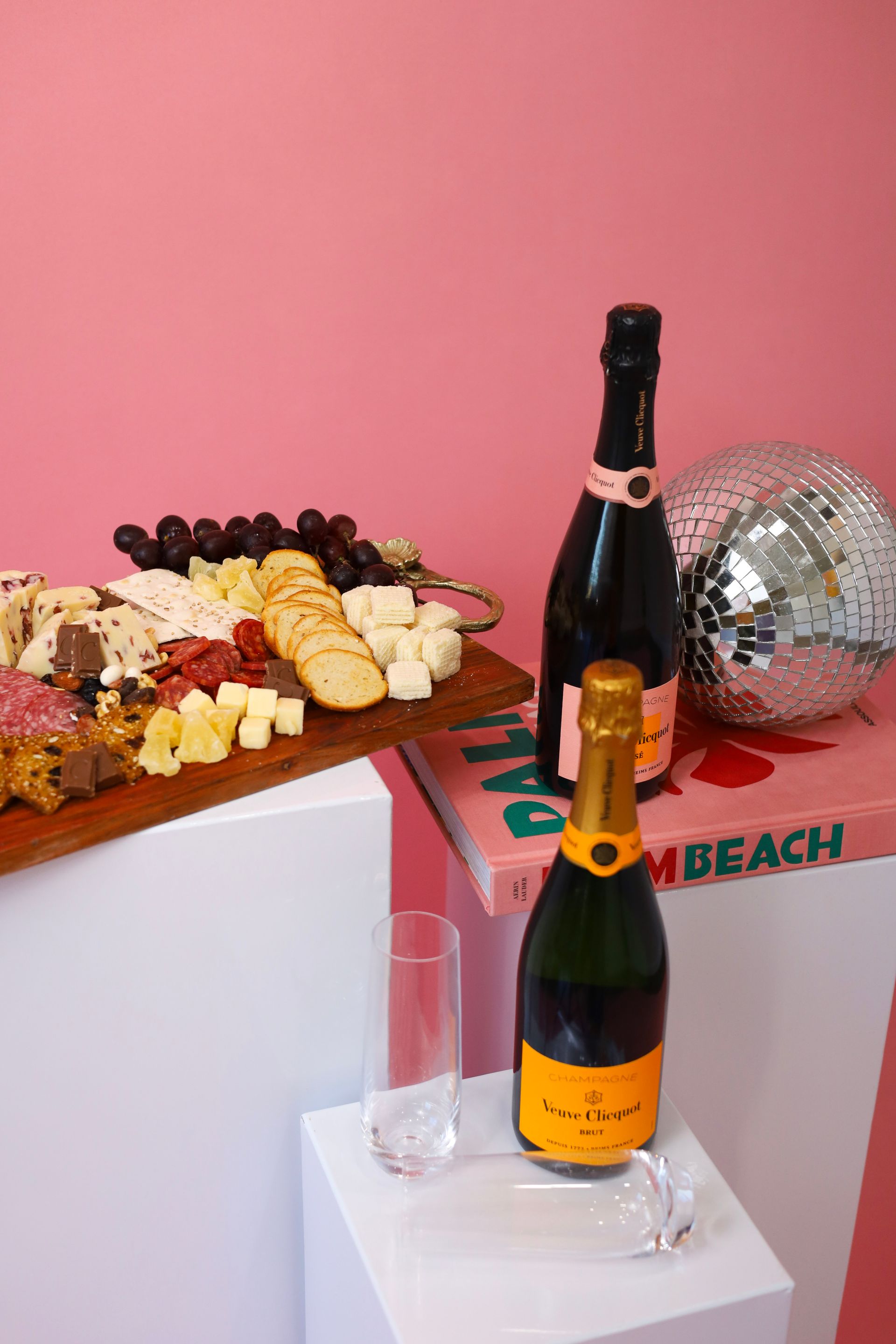 Champagne bottles and a cheese platter on a pink party table with a disco ball backdrop