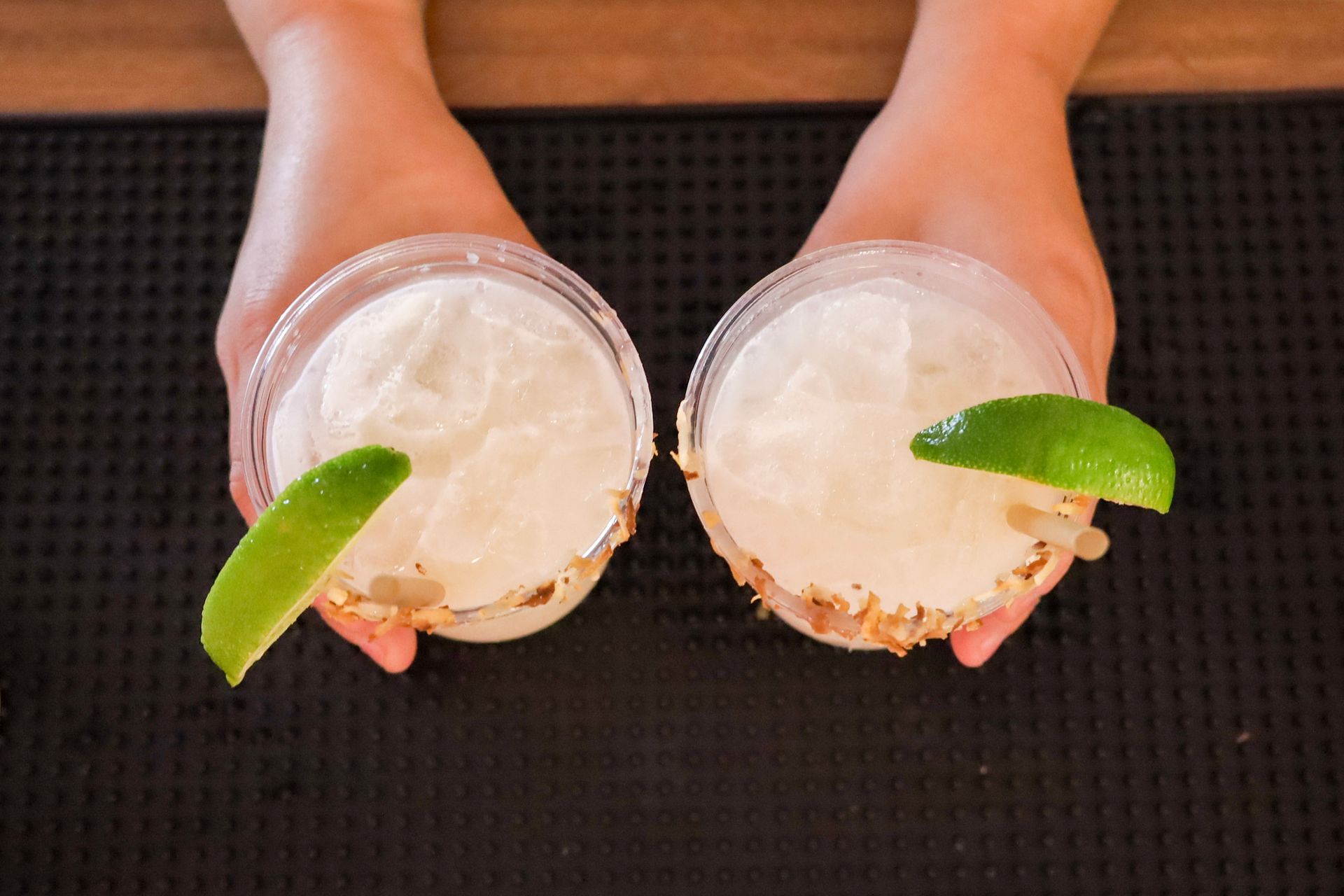 Two frosty cocktails with lime wedges held above a black mat