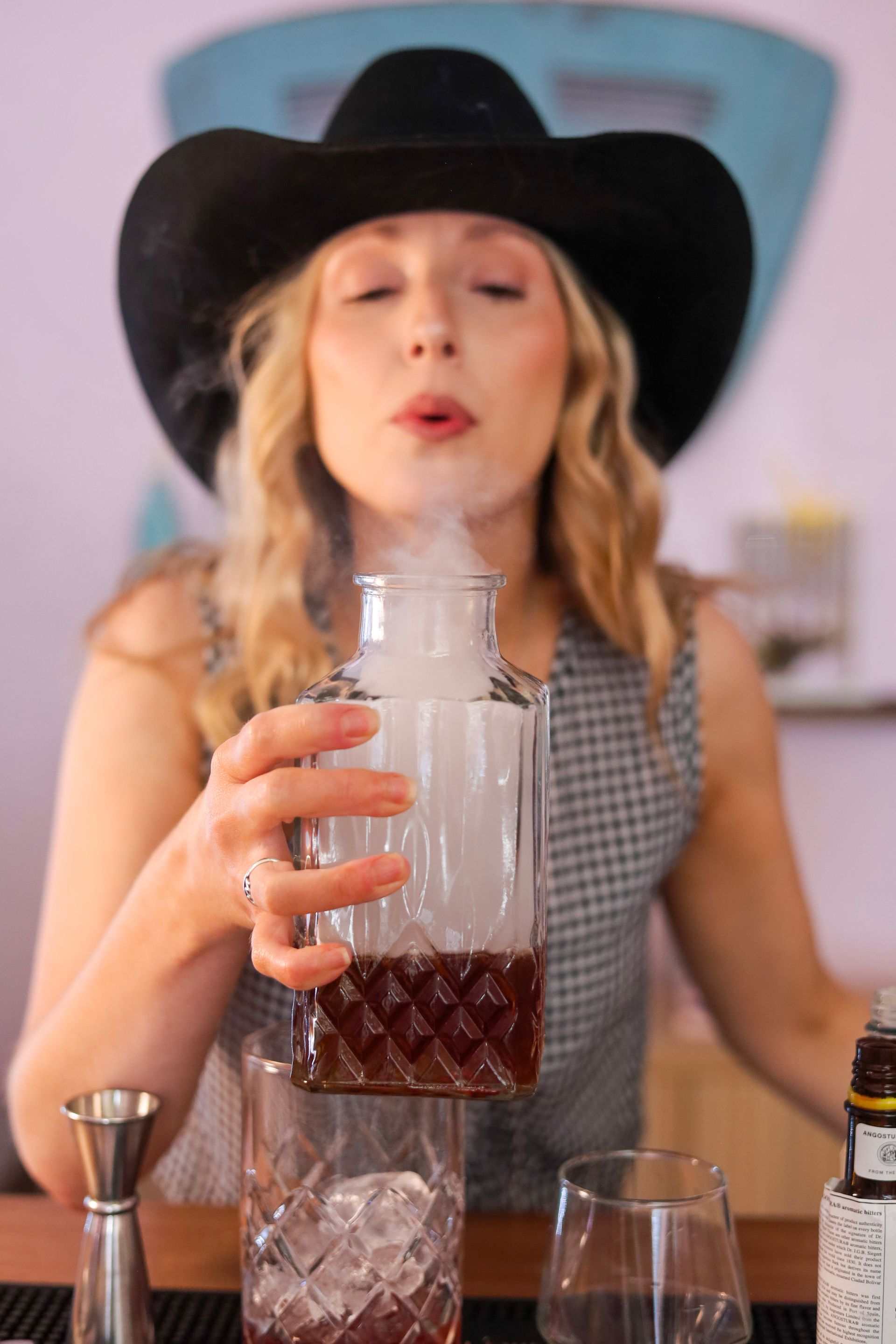 Woman in a black hat mixing a cocktail with a glass and jigger behind a bar