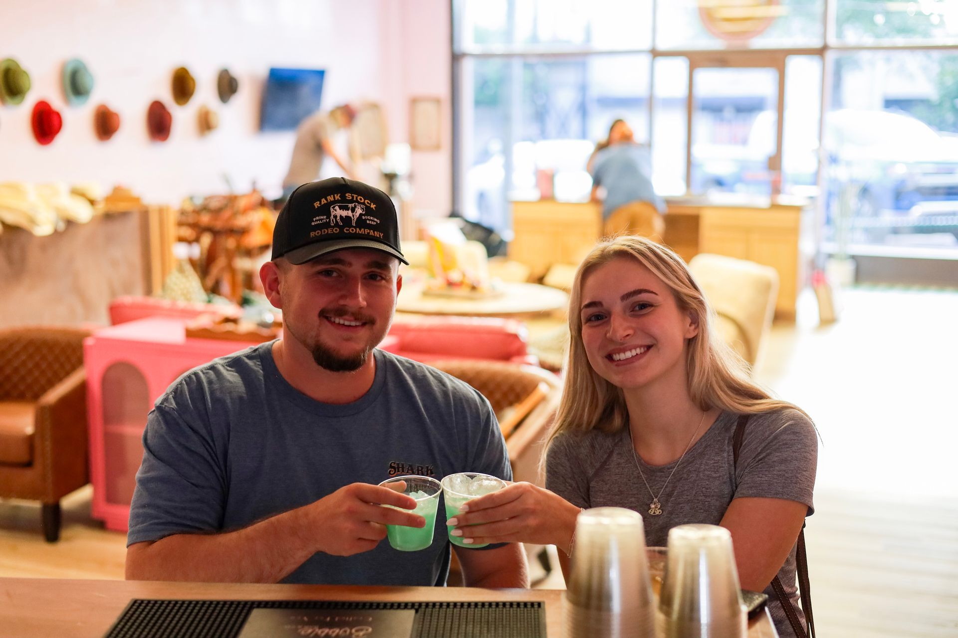 Two people smiling and holding drinks at a café table in a bright lounge.