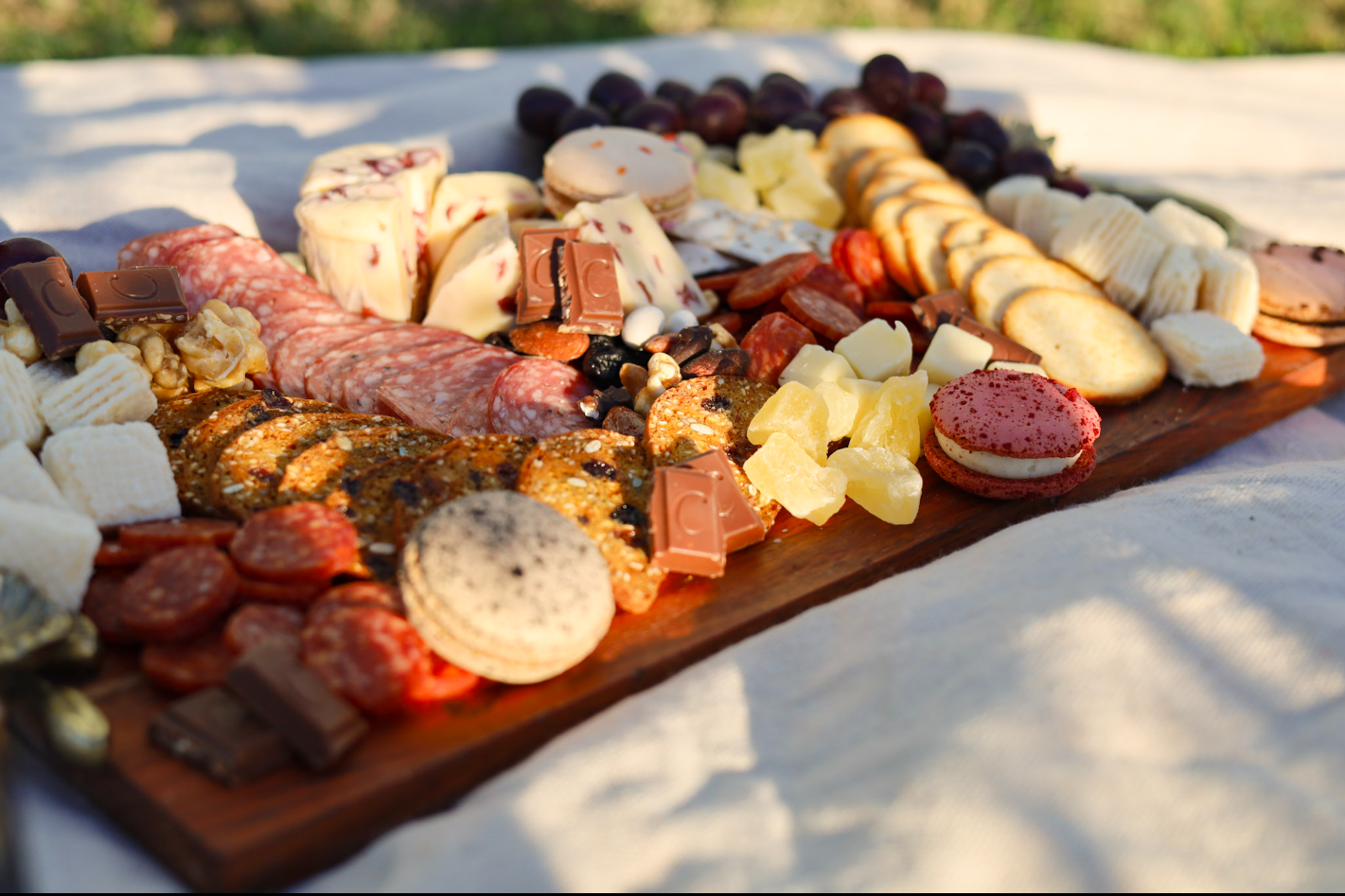 Charcuterie board with cheeses, meats, grapes, crackers, and bread on a wooden tray outdoors
