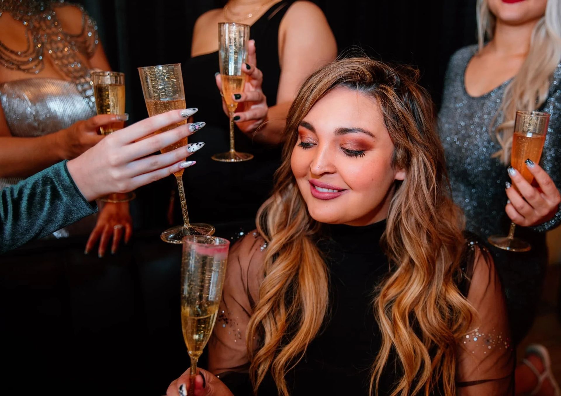 Women toasting champagne glasses at a dimly lit party, one smiling in the foreground