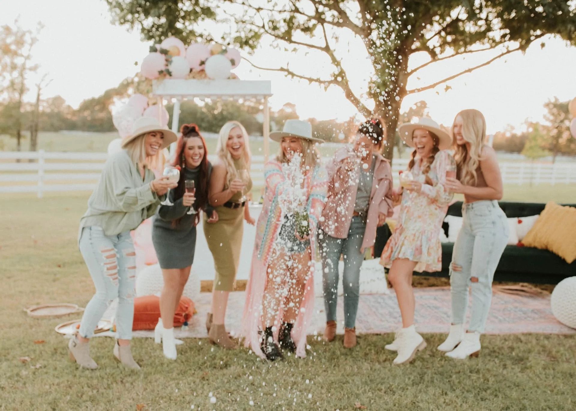 Friends posing outdoors beside a pink sparkly backdrop and balloons at a celebration