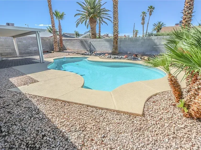 Desert backyard with a small turquoise pool, rock landscaping, palm trees, and a covered patio area.