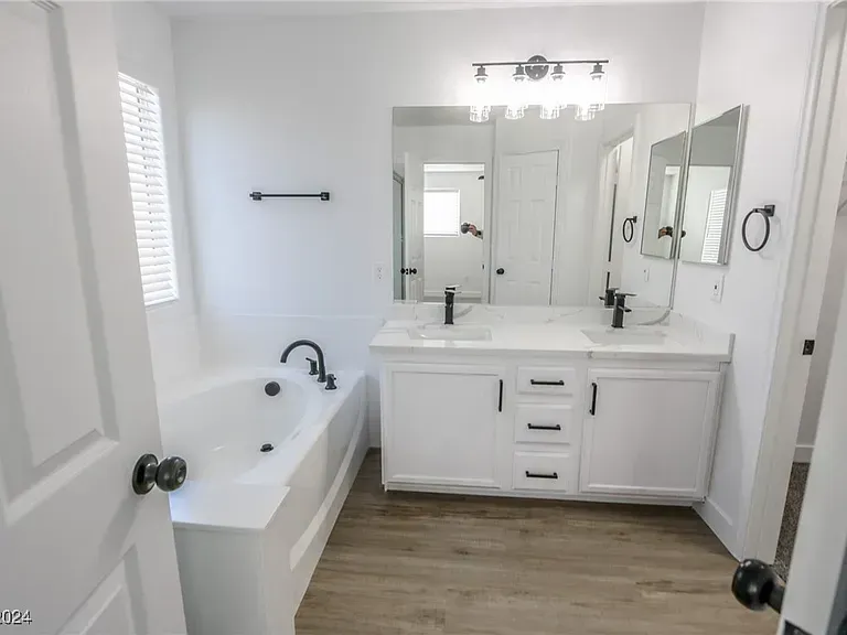 Bright modern bathroom with white vanity, bathtub, mirrors, and wood-look floor.
