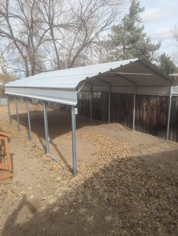 A metal carport is sitting in the middle of a dirt field.
