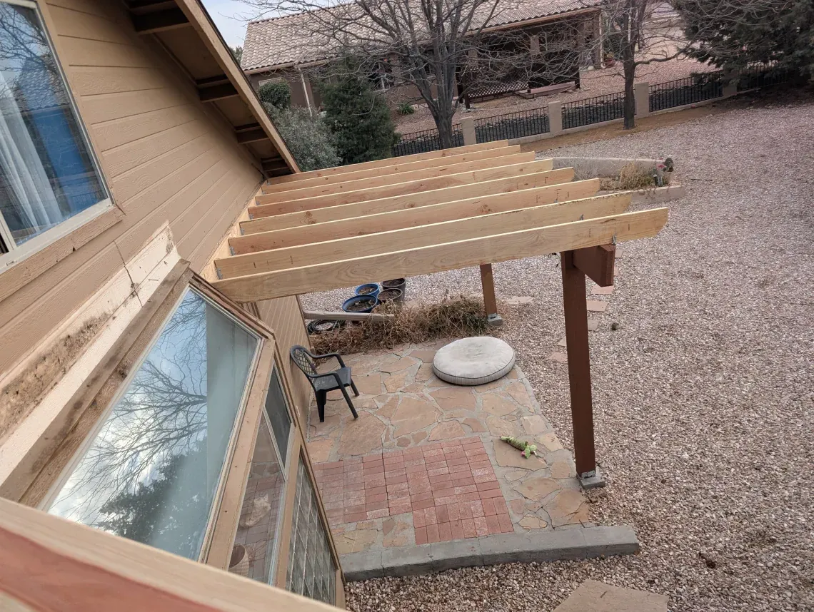 A wooden pergola is being built on the side of a house