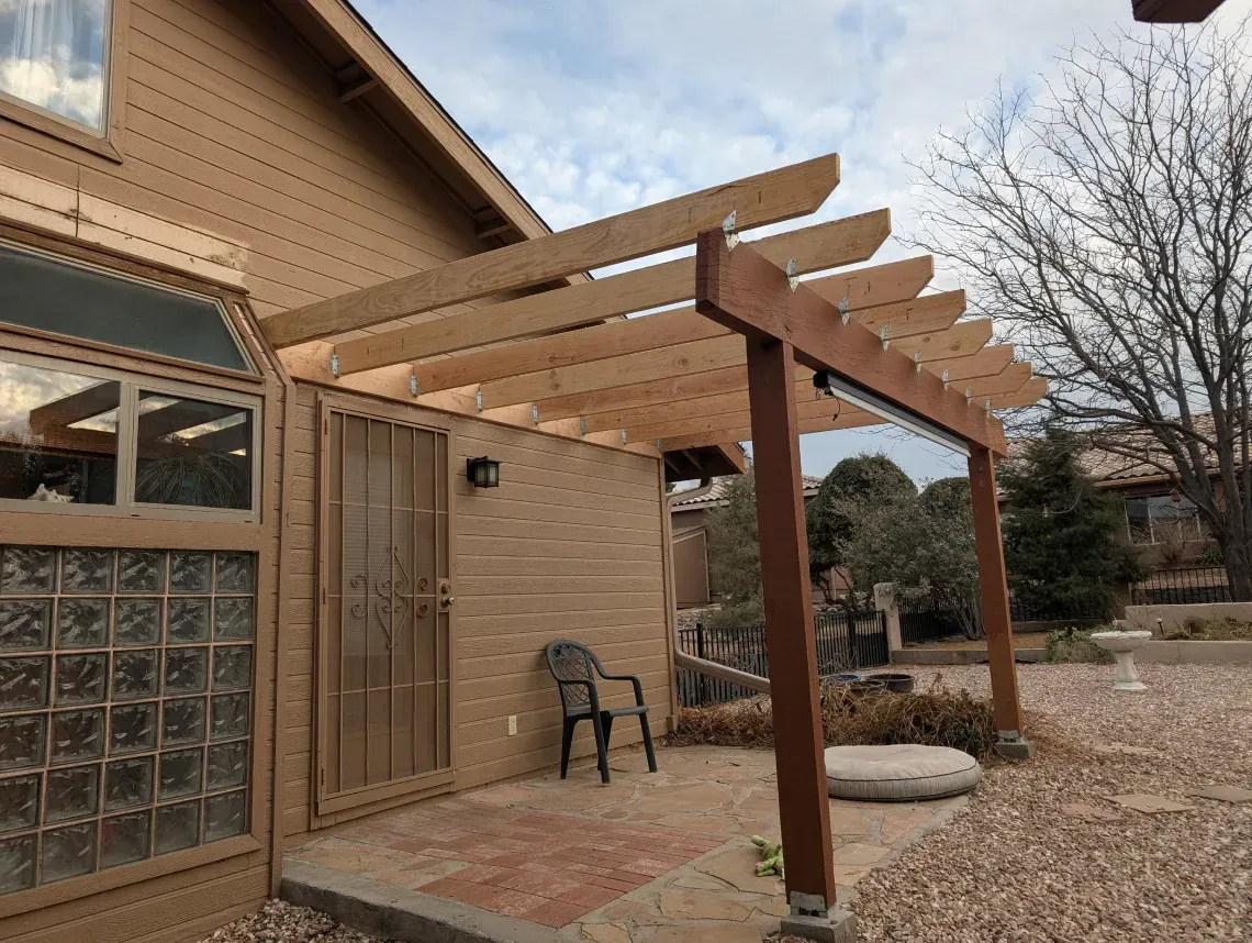 A wooden pergola is attached to the side of a house.