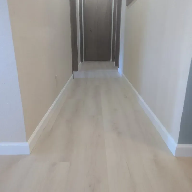 A hallway with a white wooden floor and white trim.