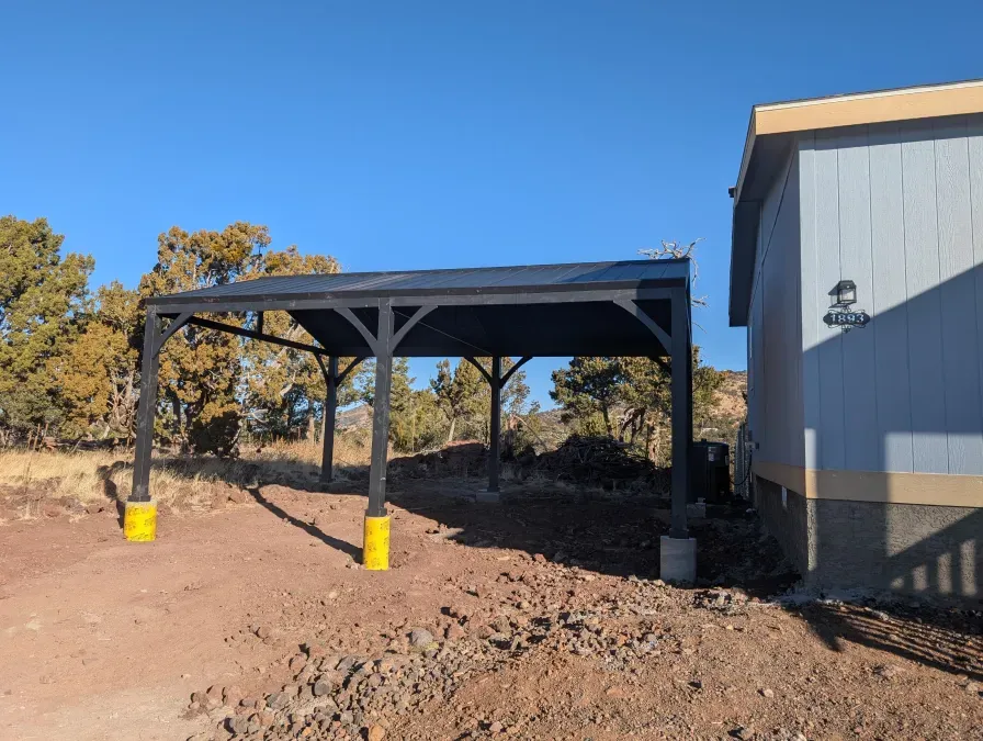 A carport is sitting next to a house on a dirt road.