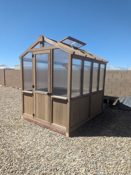 A small wooden greenhouse is sitting in a gravel area